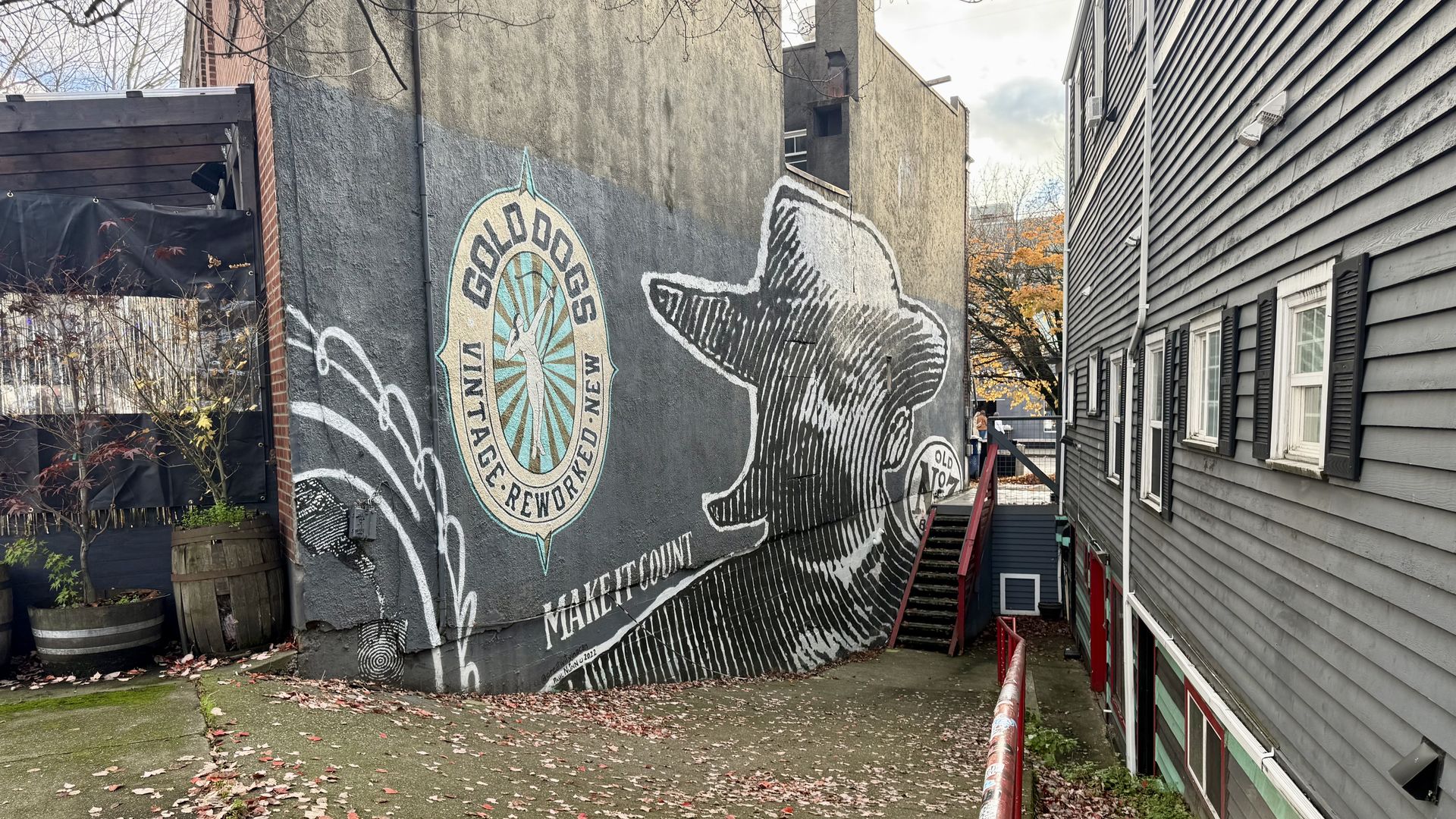 Outdoor alley wall mural of a man in a hat in black and white, text "GOLD DOGS VINTAGE REWORKED NEW" with a blue and gold emblem, and "MAKE IT COUNT" in white letters.