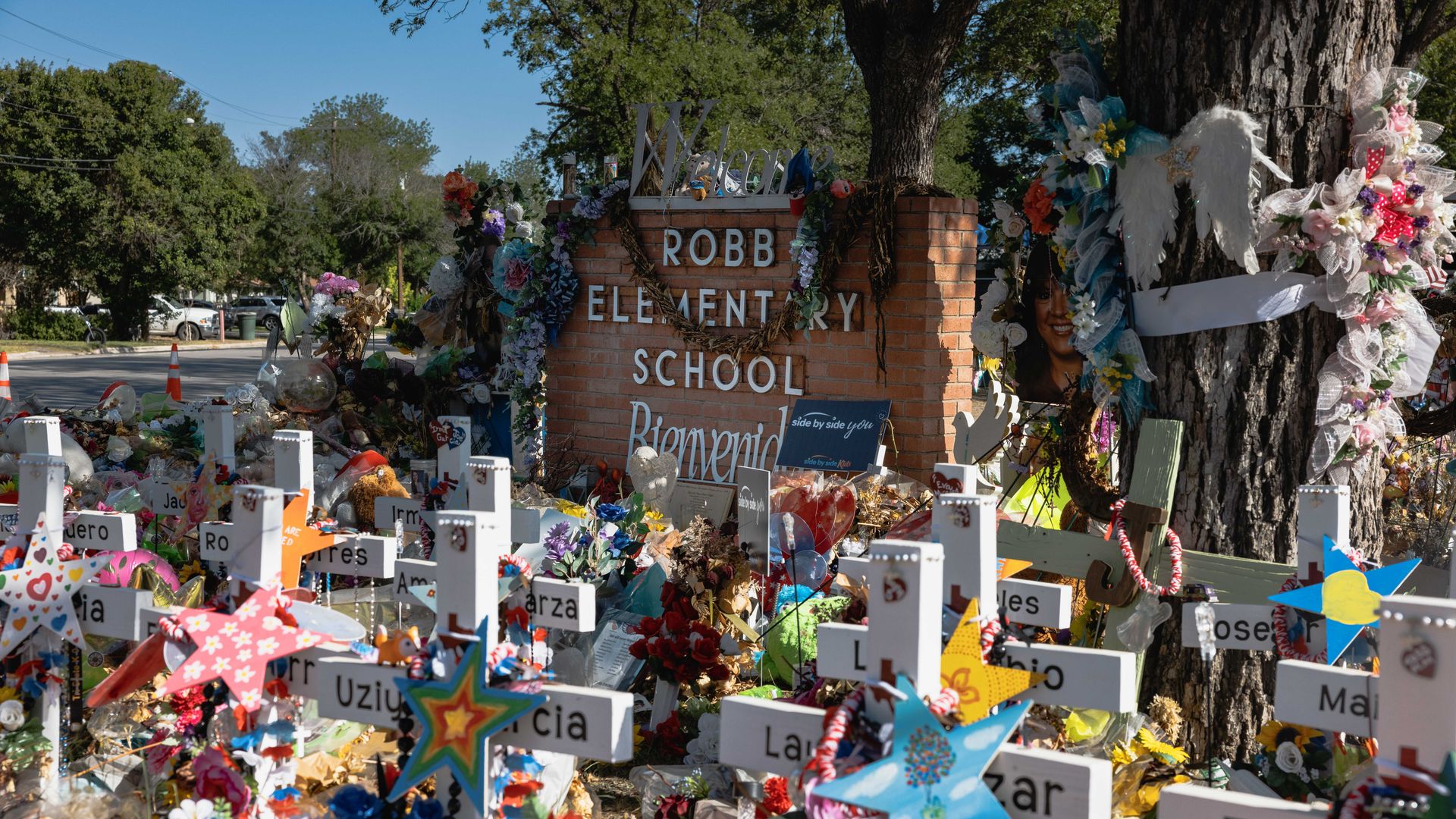 Photo of a memorial site with crosses, flowers and pictures surrounding a brick sign that says "Robb Elementary School"