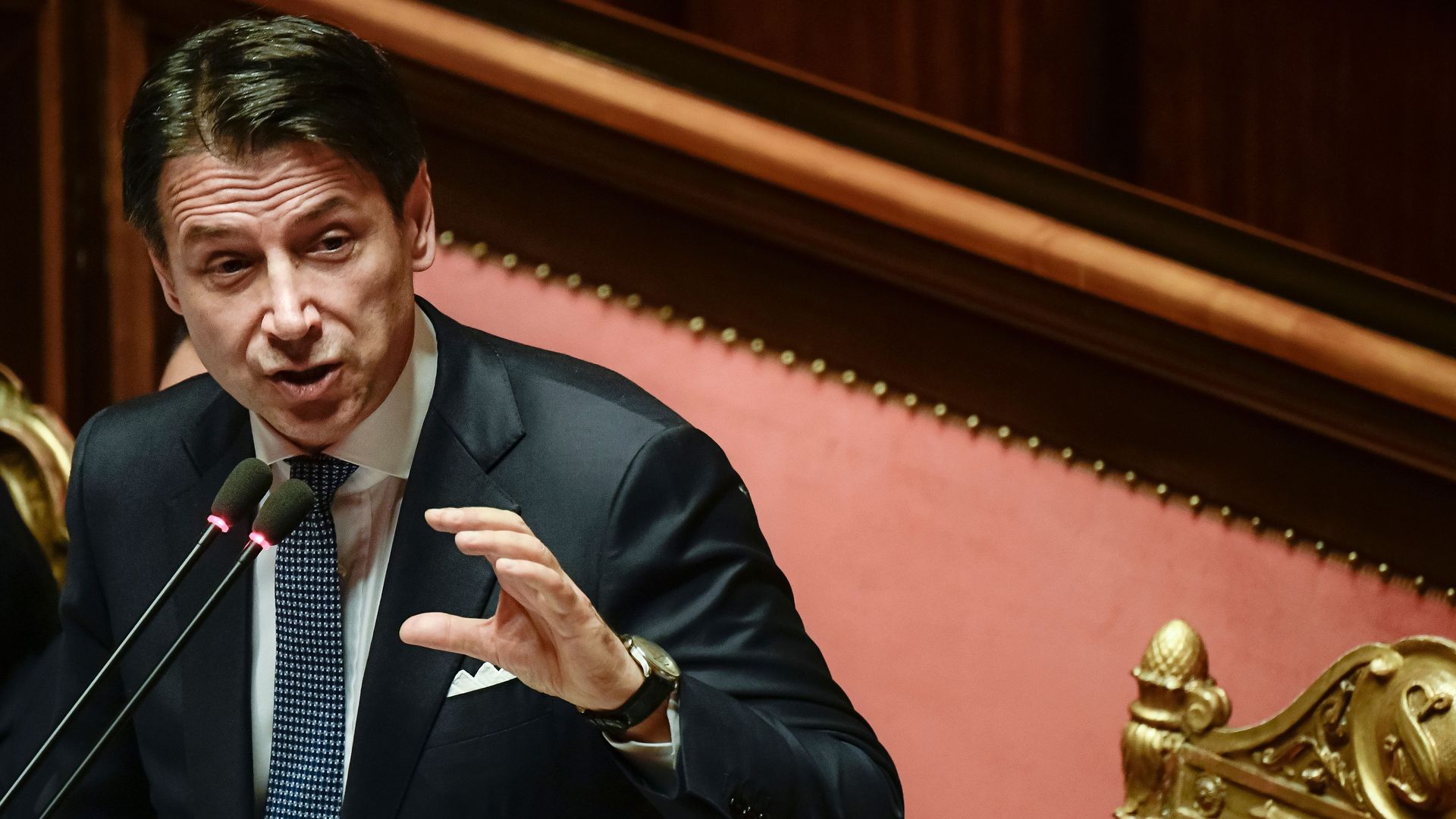 In this image, Italian Prime Minister Giuseppe Conte speaks into a microphone