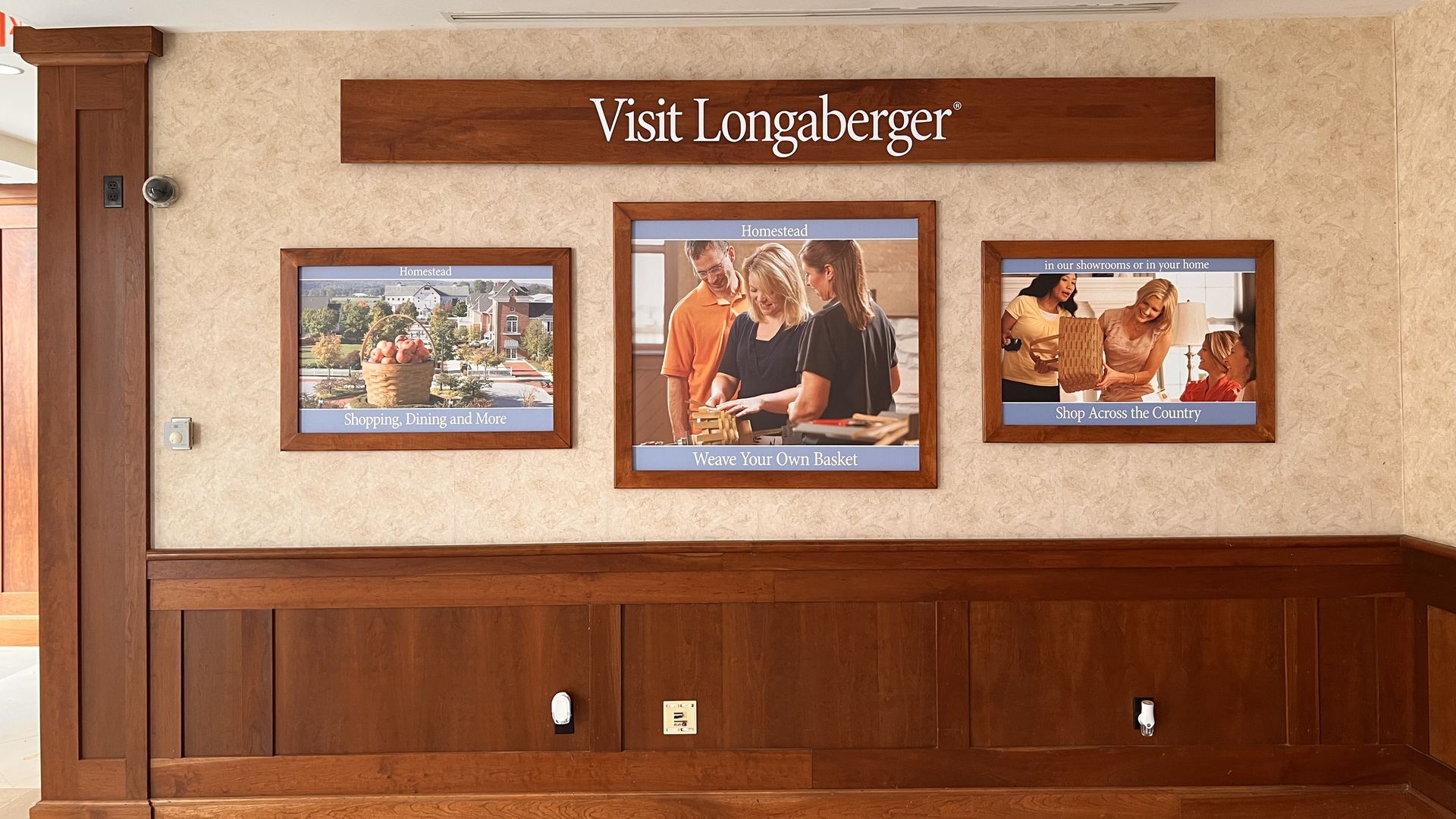 Interior wall features a long horizontal wooden sign reading "Visit Longaberger" above framed posters on a beige textured surface, with dark wood paneling and a white ceiling with recessed lights.