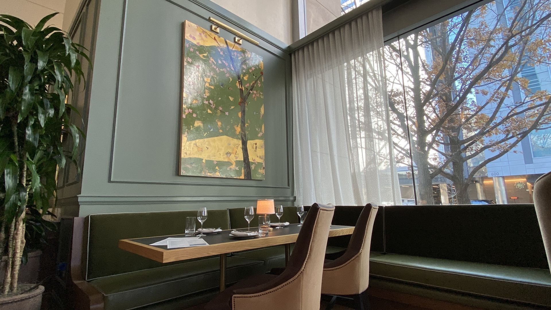 A table is set in the corner next to a painting of a dogwood tree at Dogwood in Uptown. It overlooks a window showing South College Street. 