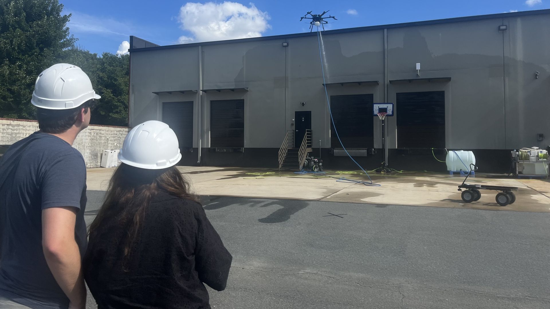 Two people in hard hats operate a power-washing drone