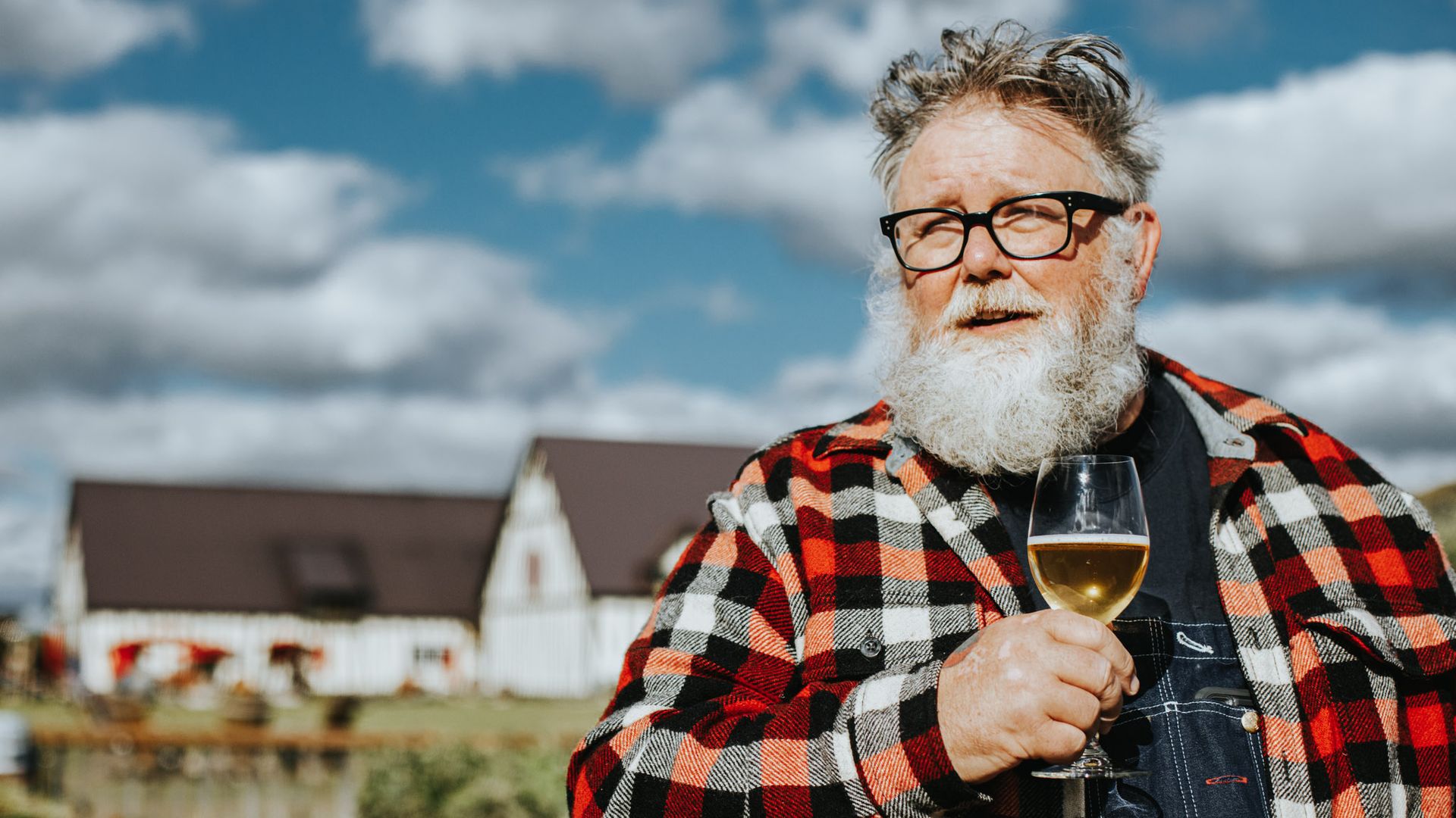 Photo of a man with a beard drinking a glass of cider on a farm. 