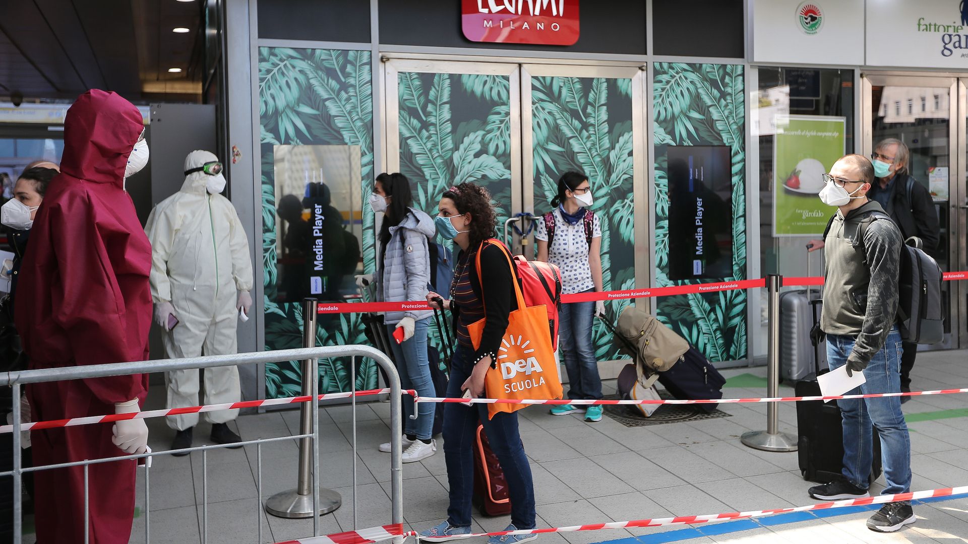 In this image, people stand in line wearing masks outside a store