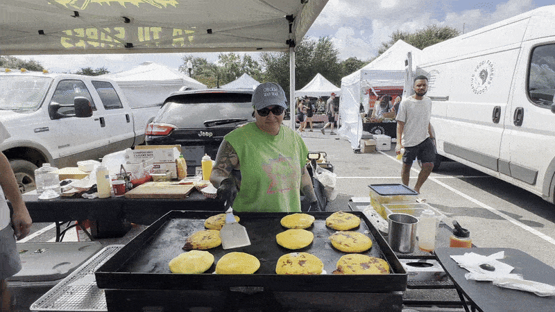 A woman flips pupusas on a black griddle.