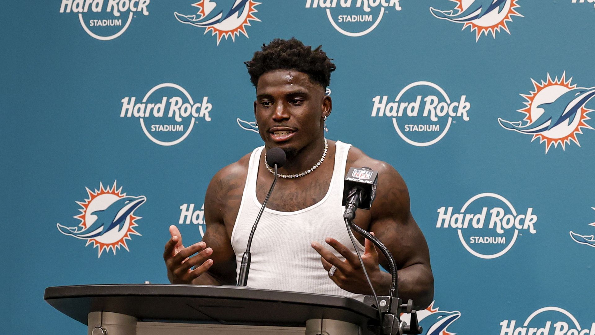 Tyreek Hill giving a press conference against a Dolphins logo backdrop. 