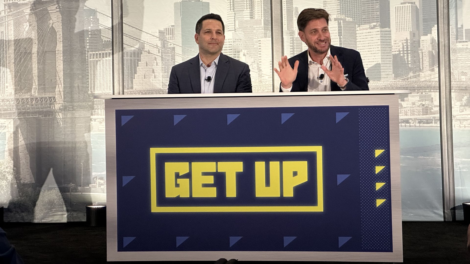 Adam Schefter and Mike Greenberg sitting behind a desk that says "GET UP"