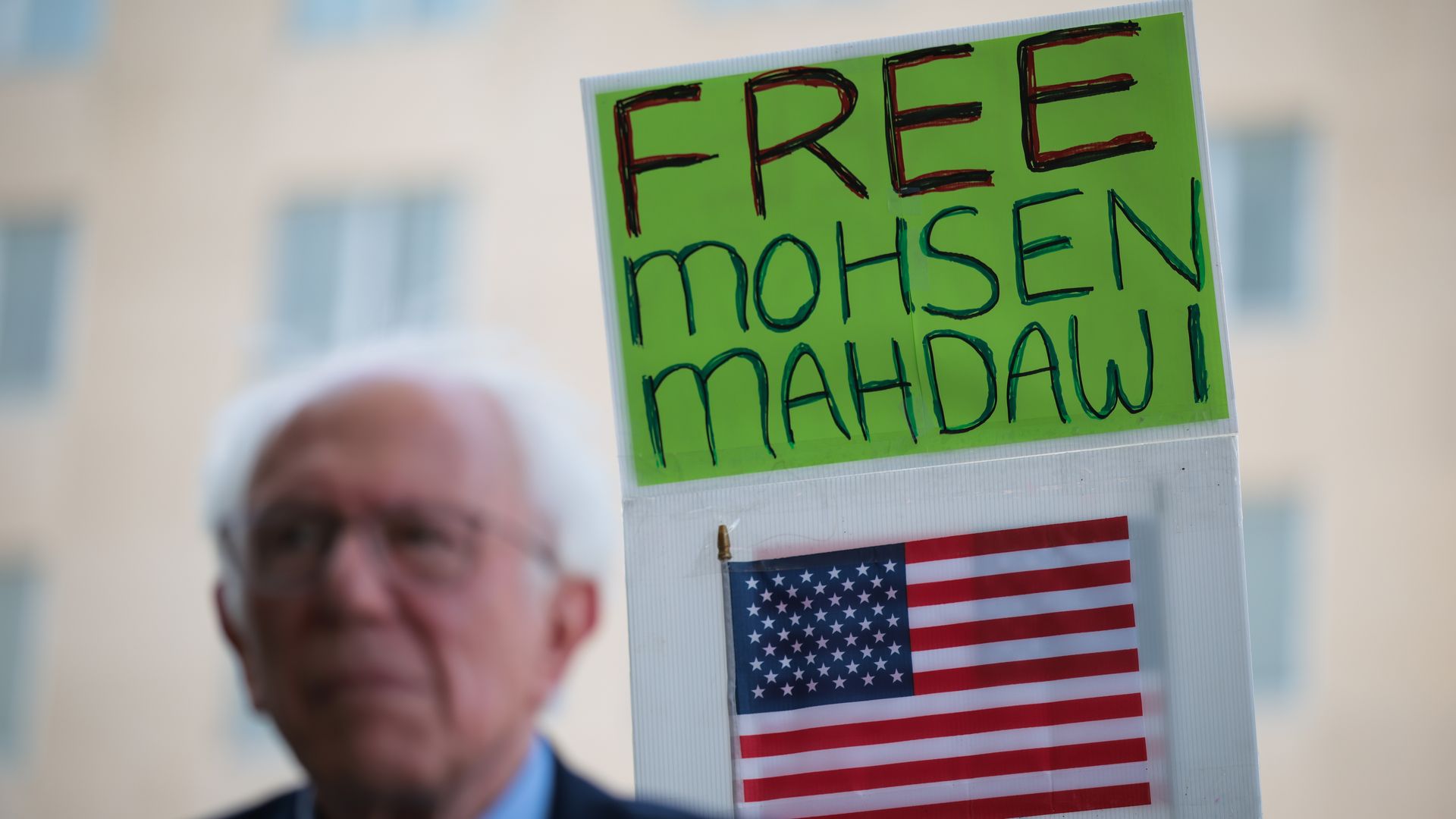 A green sign that reads "FREE MOHSEN MAHDAWI" can be seen behind Bernie Sanders.