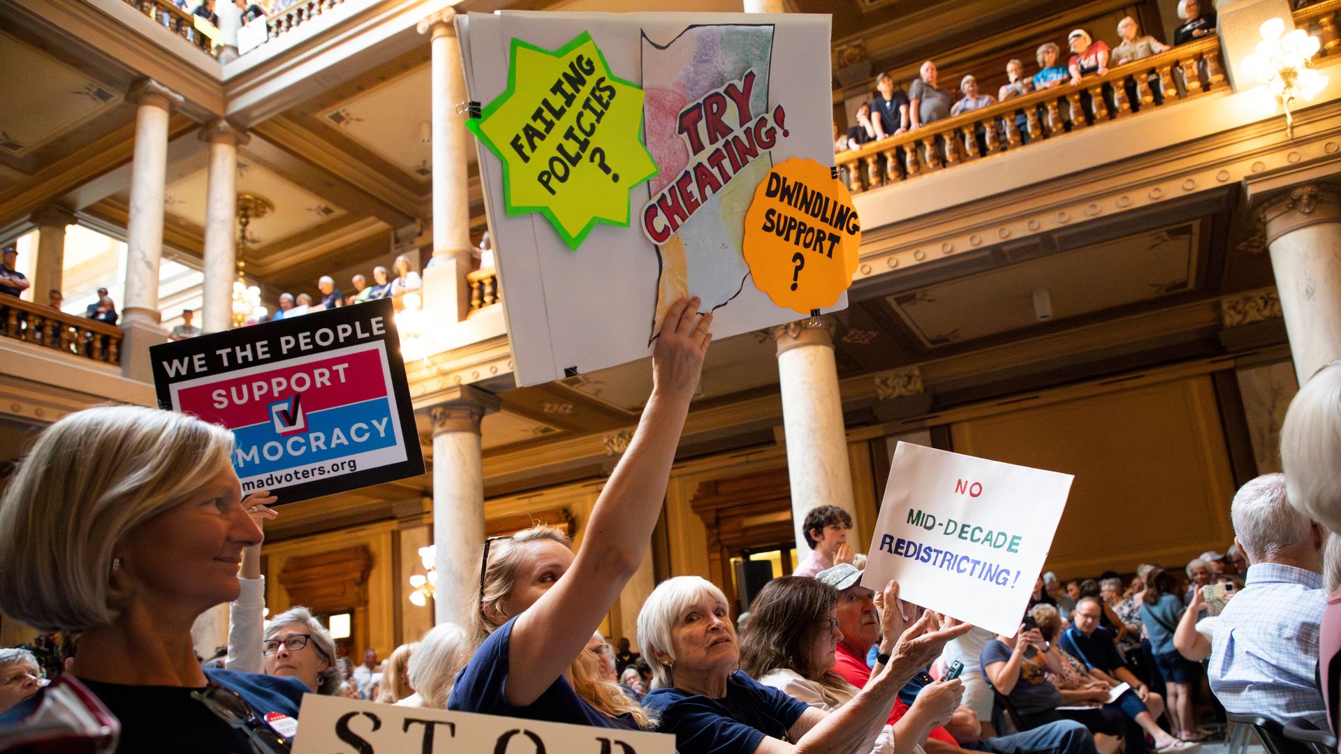 Protesters hold anti-redistricting signs, one of which reads, "FAILING POLICIES? TRY CHEATING" inside the Indiana statehouse.