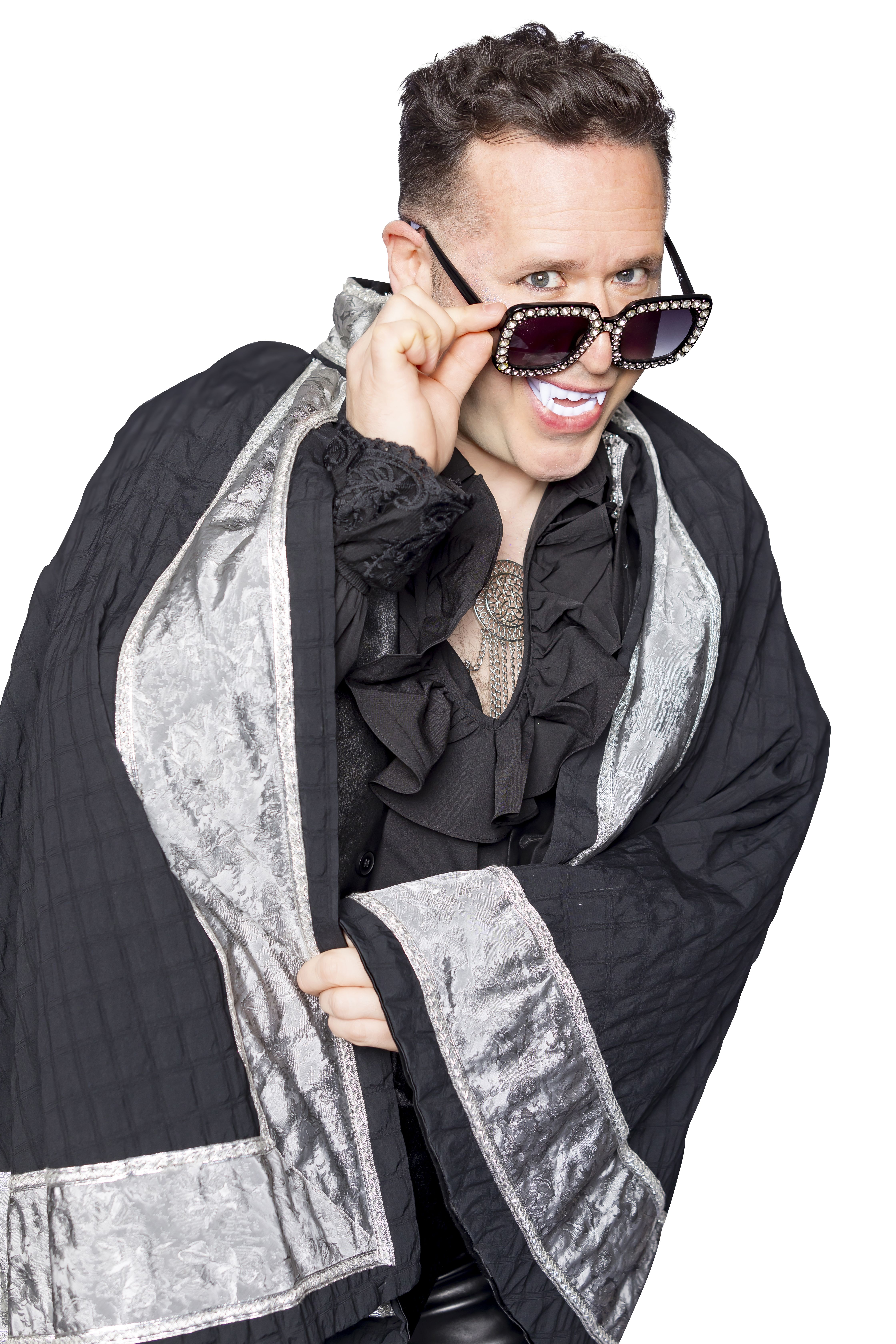 An actor dressed as Dracula peers over his glasses.
