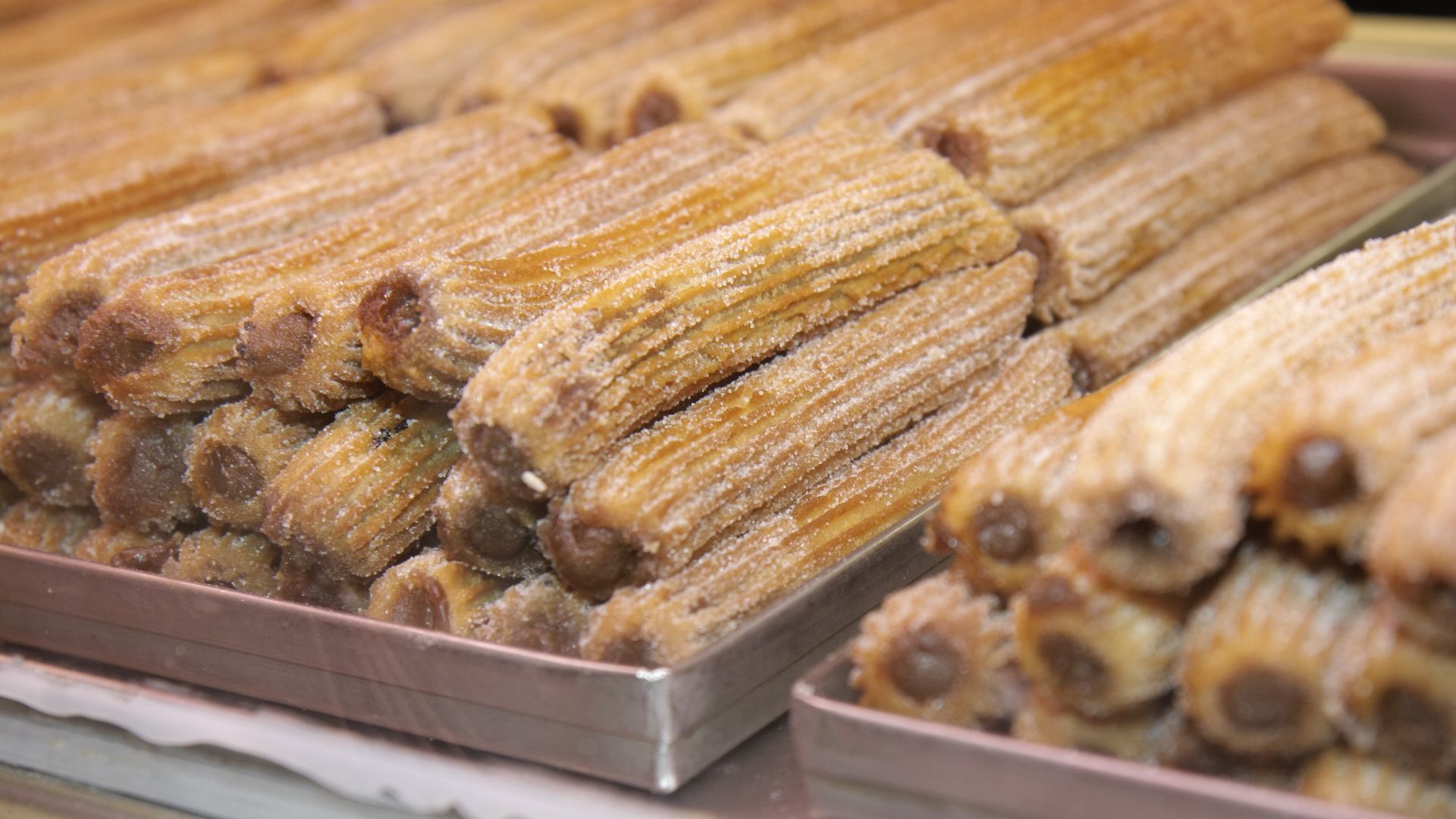 A batch of churros from Churros Manolos sits behind display glass.