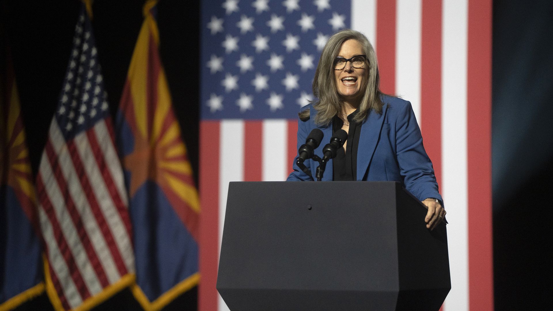 Governor Katie Hobbs at a podium with Arizona and U.S. flags in the background.