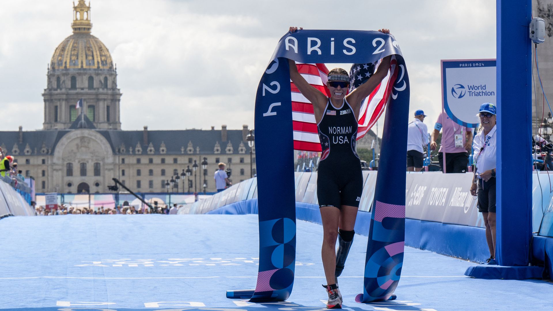 Grace Norman poses on the Pont Alexandre III with a banner that says "Paris 2024" and an American flag