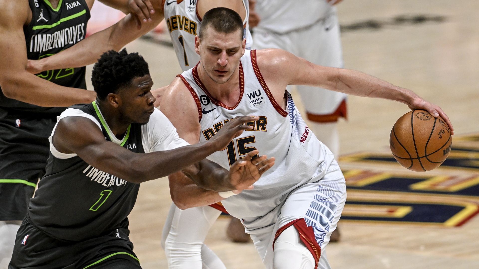 A man in a white jersey with red trimming handles a dark orange basketball while pushing away another man in a black jersey with lime green trimming during a basketball game. 