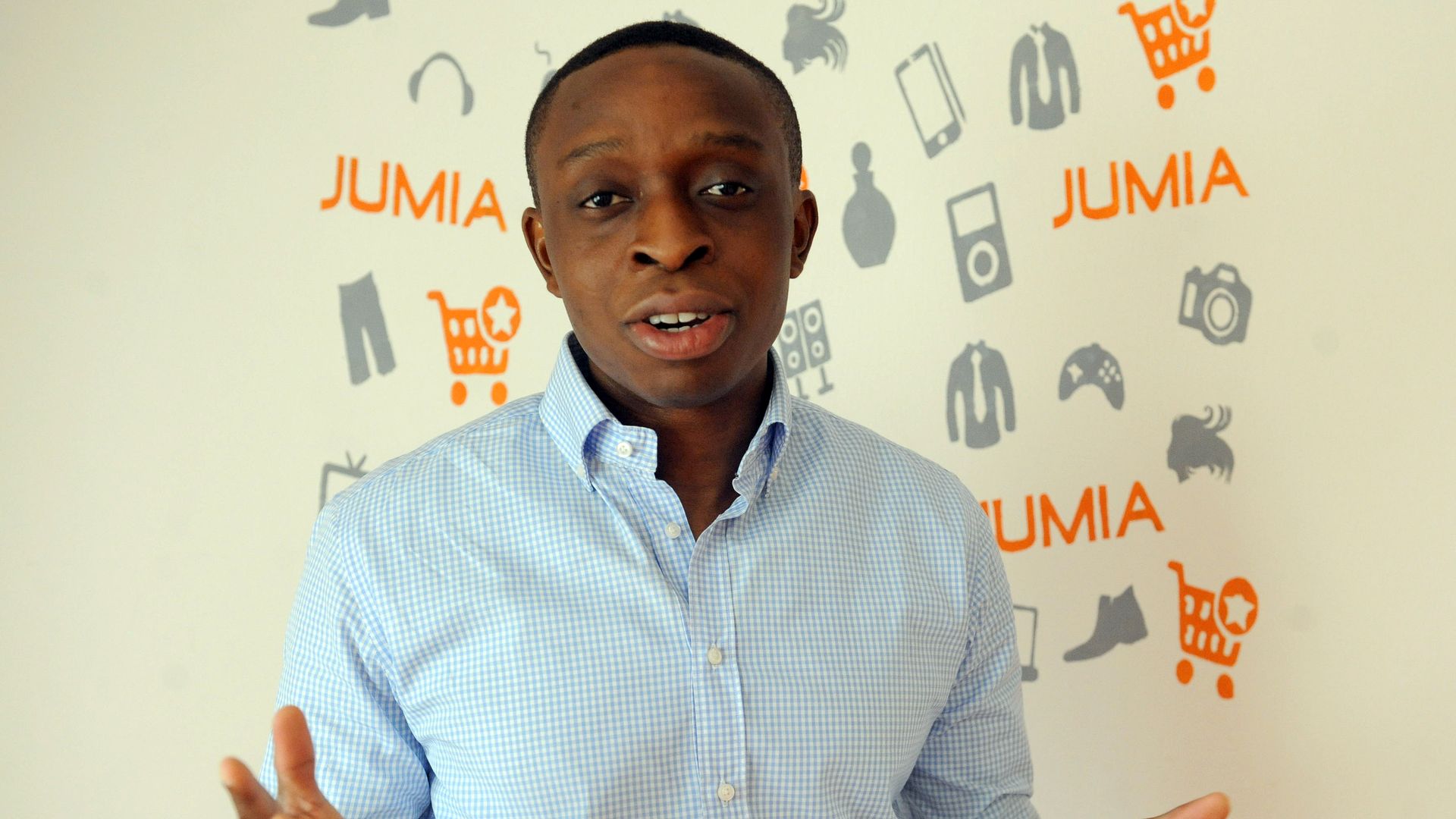 Co-founder of Jumia, Tunde Kehinde, stands and speaks in front of a wallpaper that displays the Jumia logo.