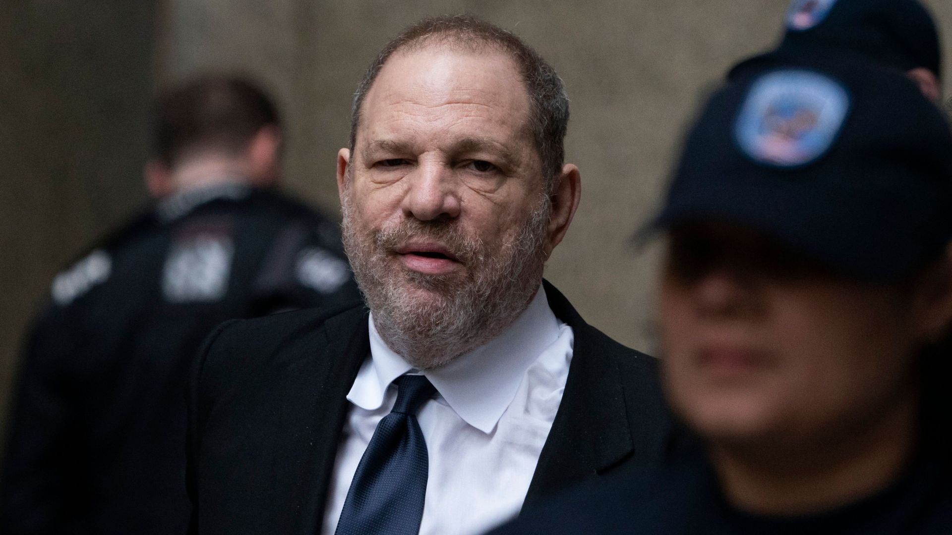 In this image, Harvey walks in a tie surrounded by police.