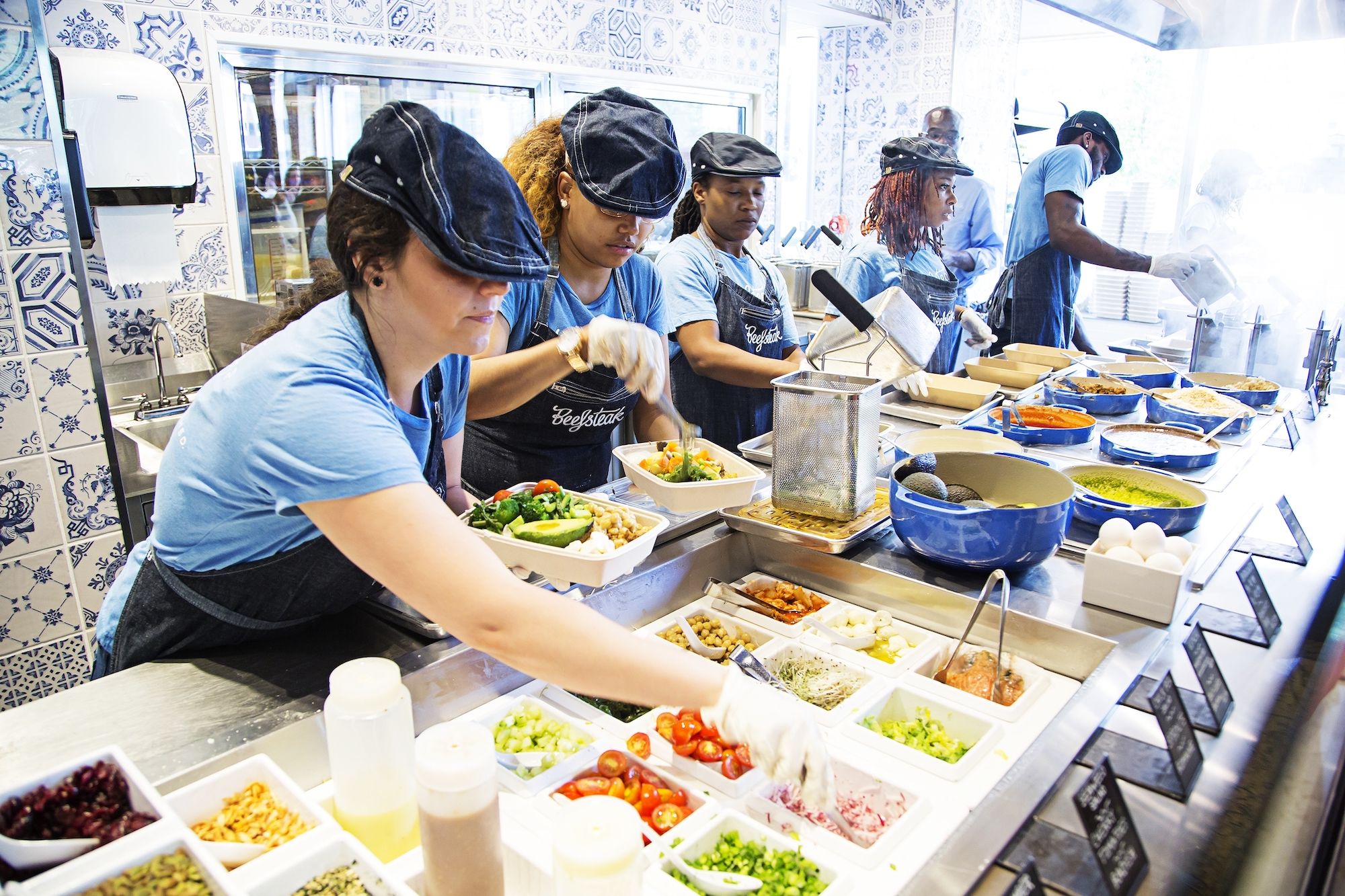 A group of workers in blue t-shirts and denim caps plate bowls of vegetables at Beefsteak Restaurant in Washington, DC. (Photo by Scott Suchman/For the Washington Post)