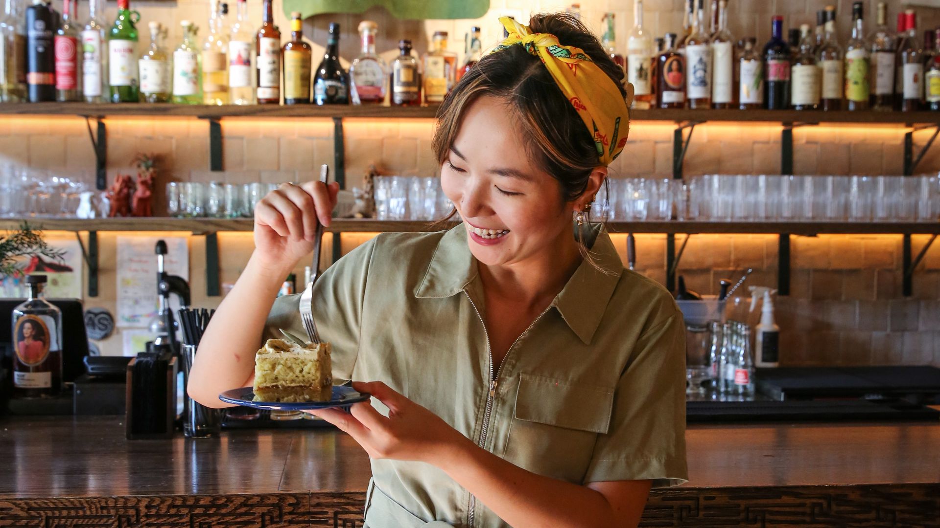 A woman eats a piece of cake behind a bar