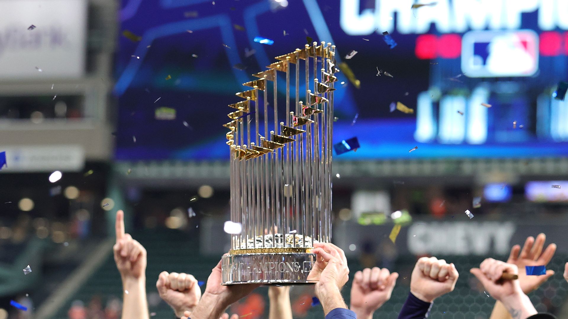 Hands hold up the Commissioner's Trophy, the two-foot tall sterling silver trophy featuring 30 flags of baseball teams that is awarded to the World Series winners
