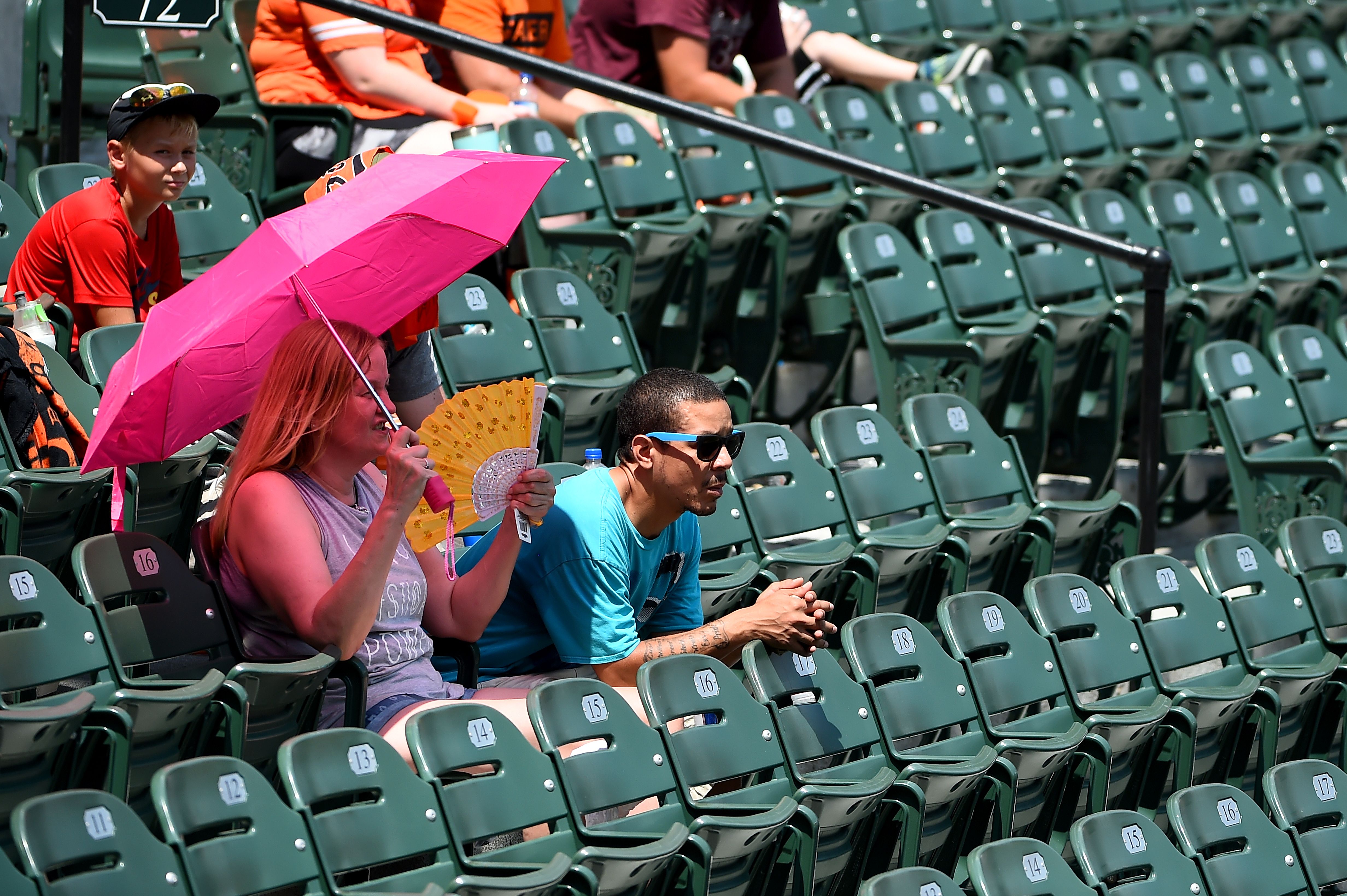 Fans try to cool off under an umbrella during the game between the Baltimore Orioles and the Boston Red Sox at Oriole Park at Camden Yards on July 21, 2019 in Baltimore, Maryland.