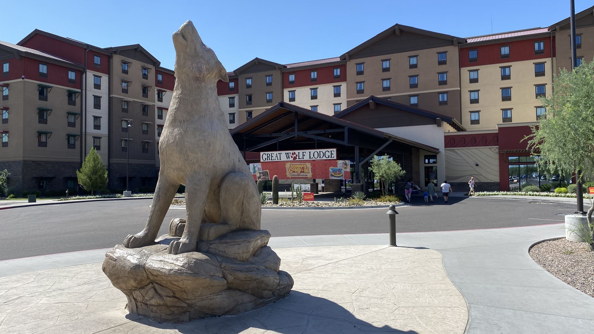 A statue of a howling wolf in front of a large hotel.