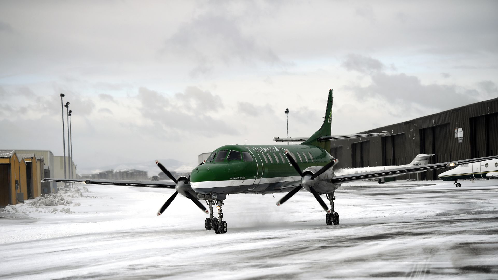 A green airplane seen at a snowy airport. 