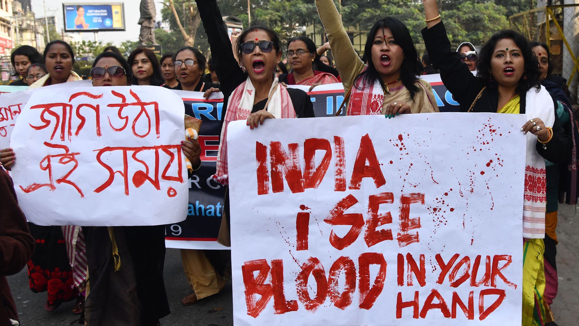 Women protesting in India hold a sign that says "India I see blood in your hands."