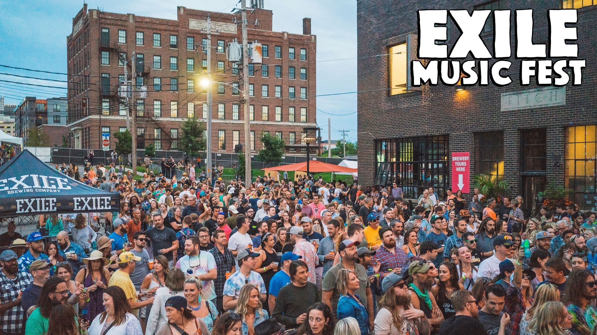 A crowd of people listen to music on a sign for the Exile Music Fest