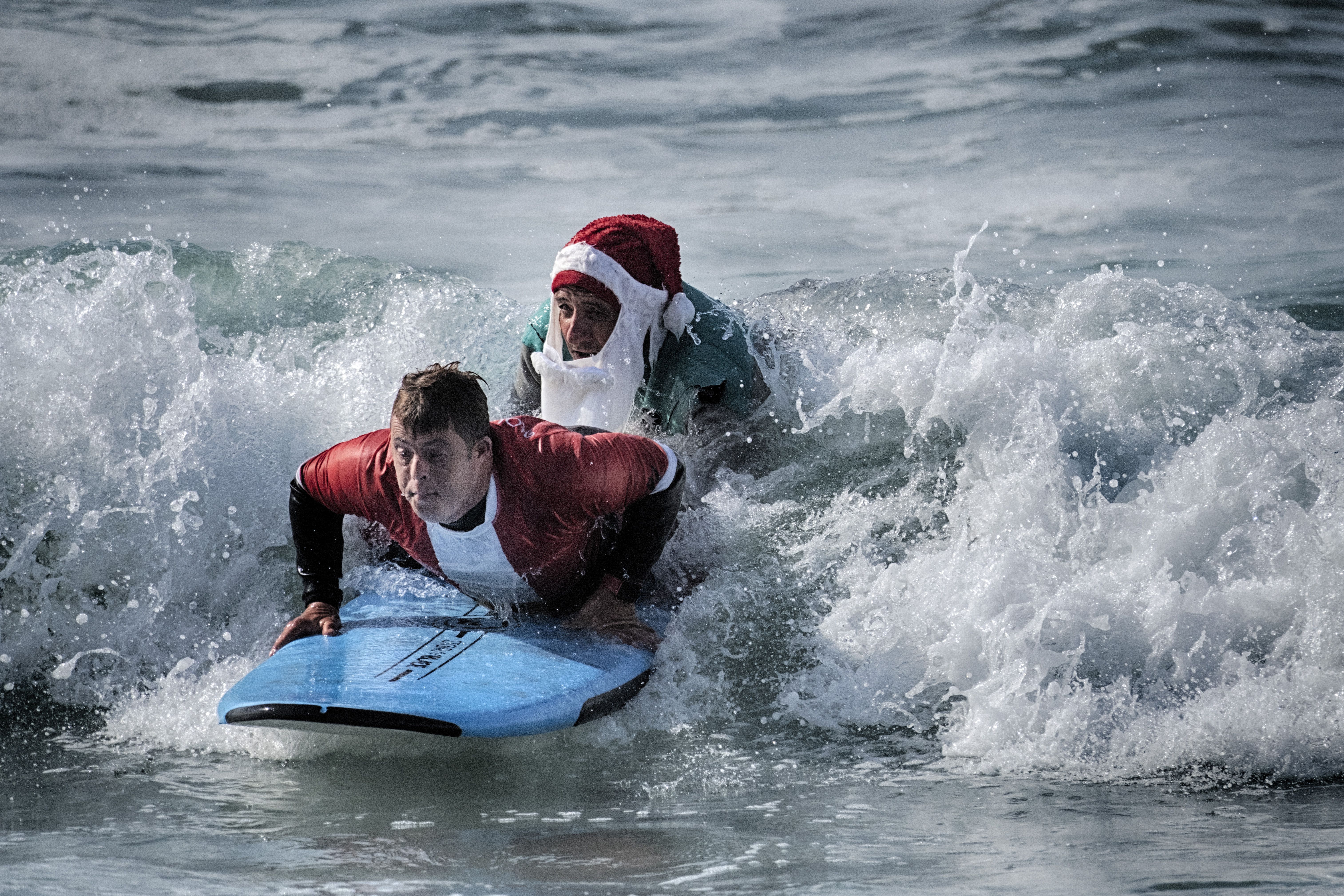 Mark Gabriel, right, dressed as Santa Claus, helps surfer Creighton Wall who suffers from Down Syndrome during the Surfing Santa event in Dana Point, Calif. on Sunday, Dec. 8, 2024. (AP Photo/Richard Vogel)