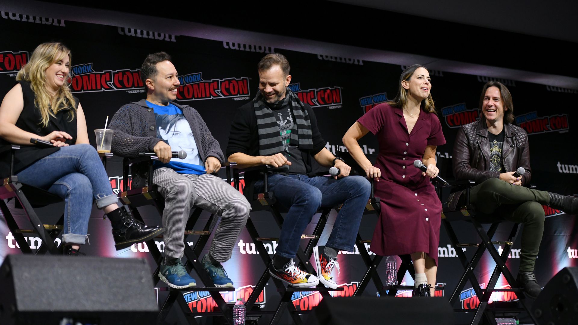A group of individuals take seats on a stage with "San Diego Comic Con" on a banner in the background. It is the cast of the Dungeons and Dragons show Critical Role.