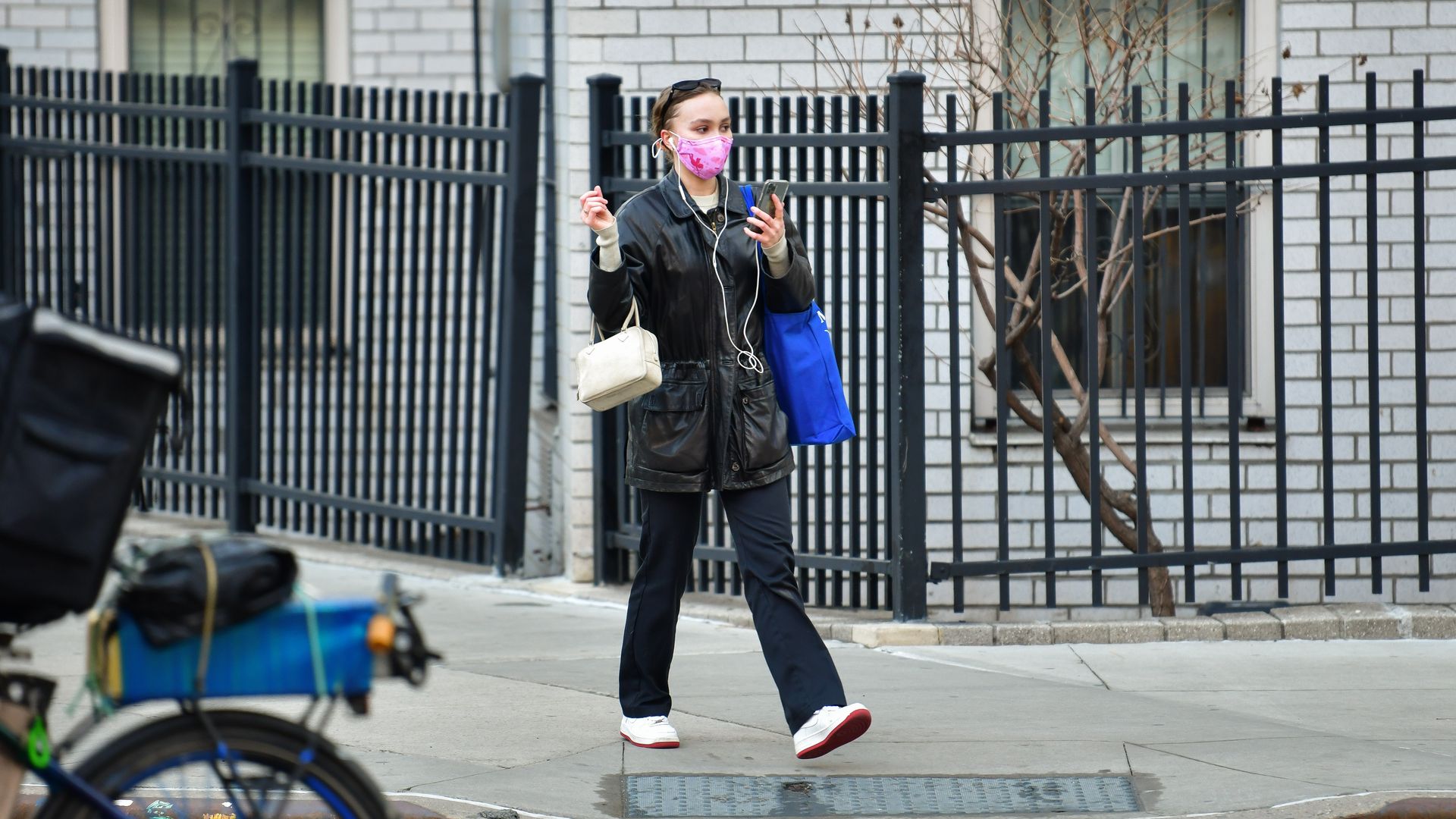 A woman walking down a city street sidewalk wearing wired headphones.