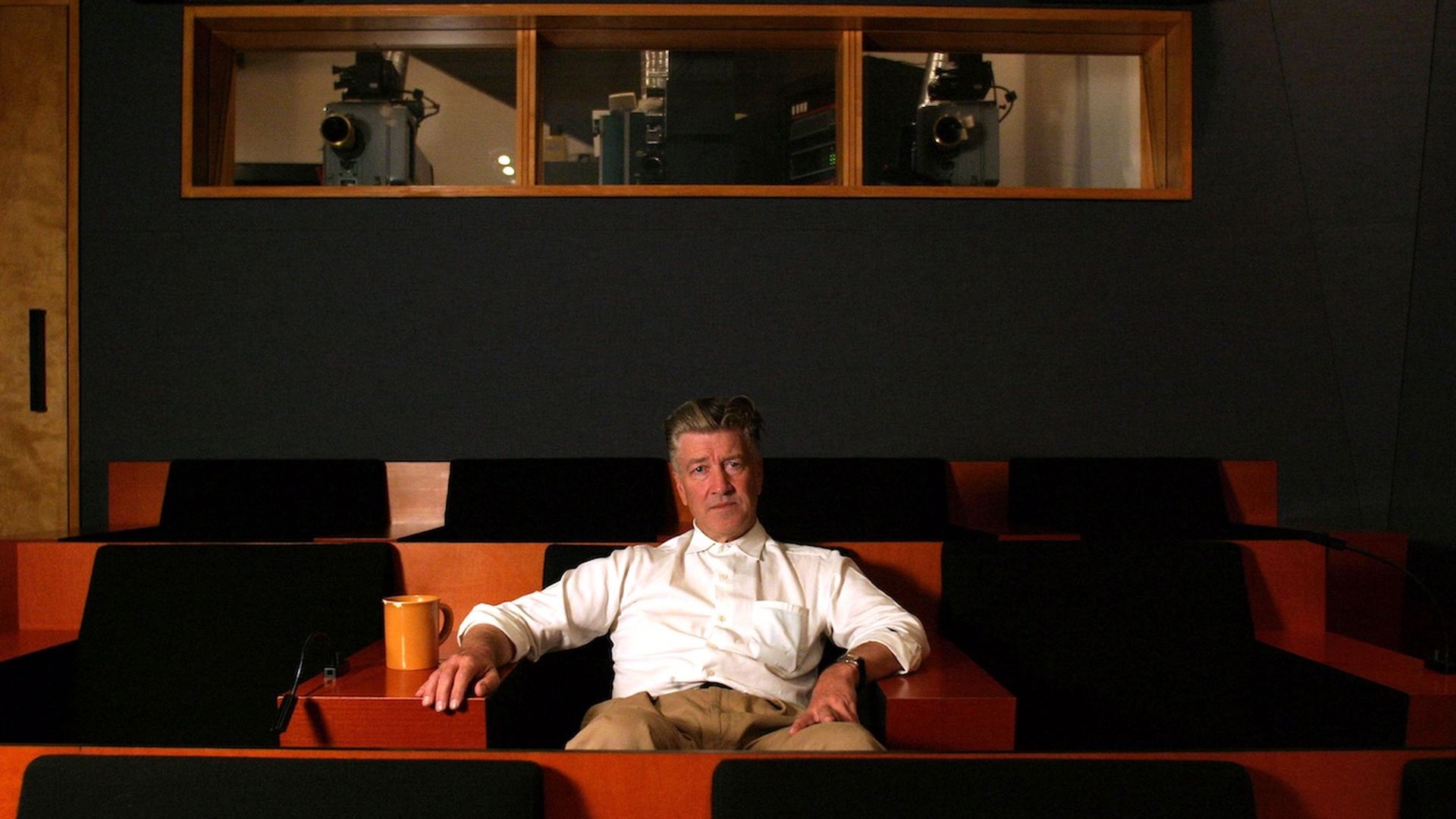 A photo of a person sitting in a movie theater, with red seats, and a beverage next to them.
