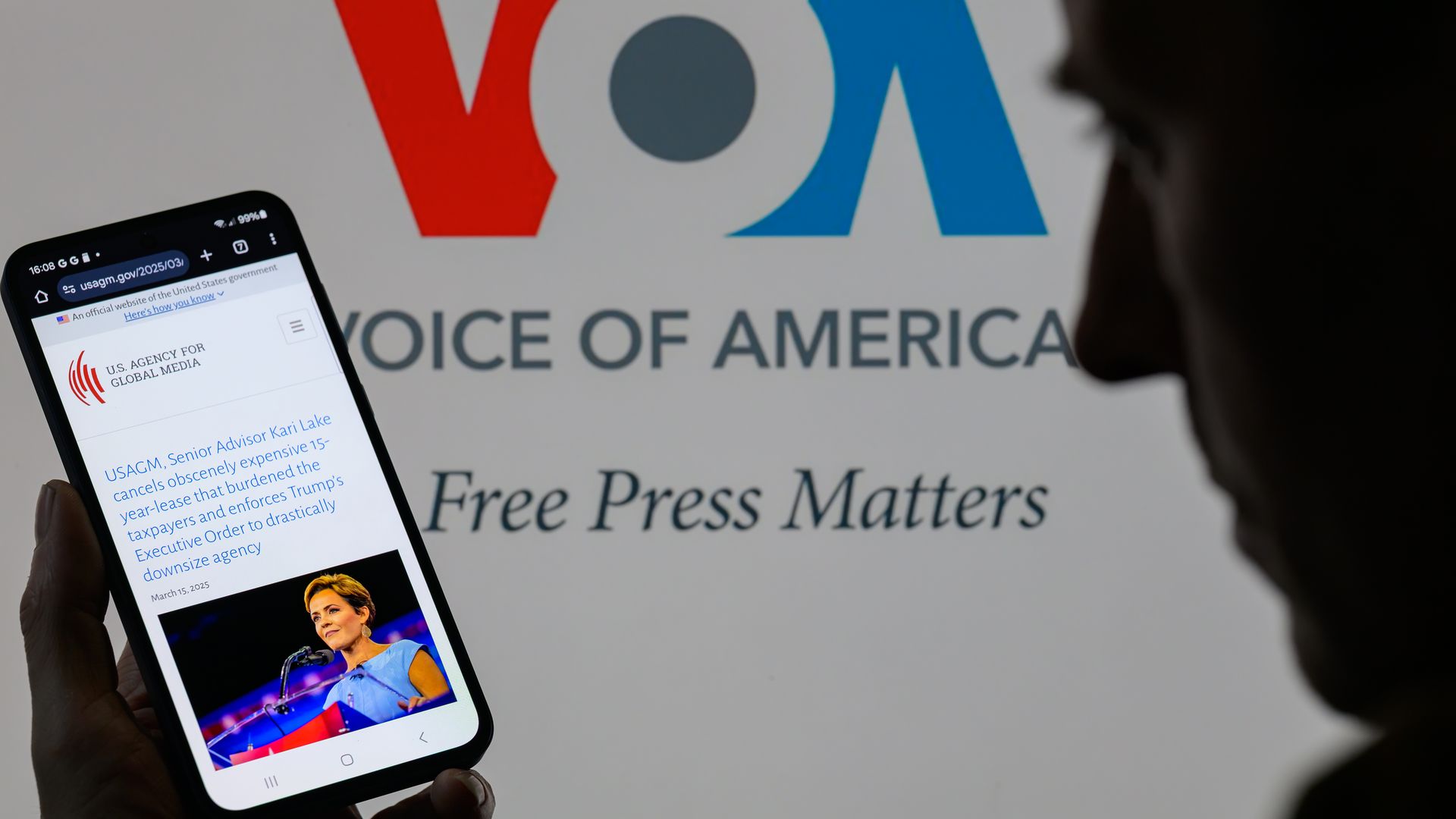 A phone screen showing an article with a photo of Kari Lake in front of a Voice of America sign.