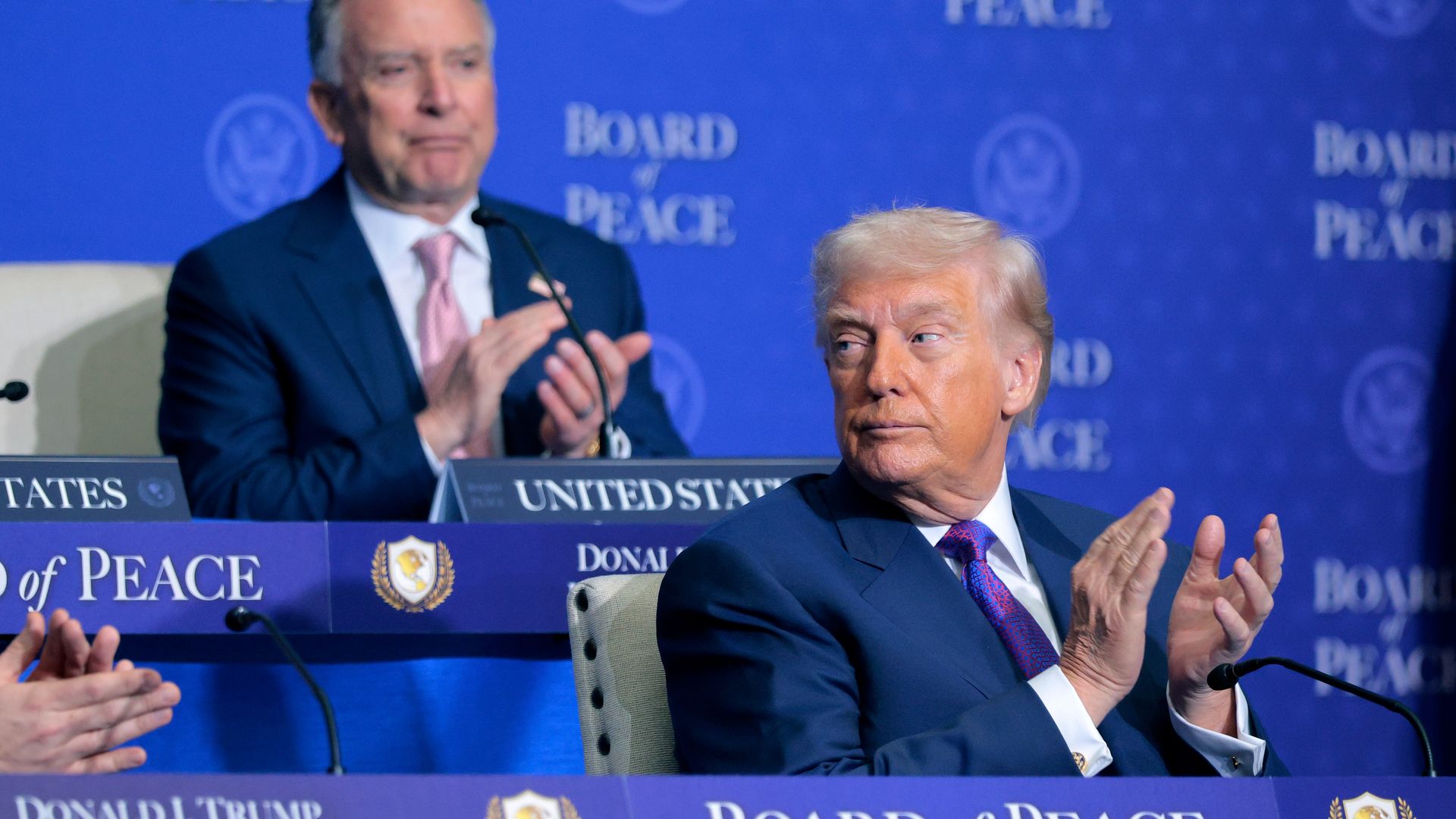 President Trump and Special Envoy Steve Witkoff clap at a meeting table during the Board of Peace inaugural session in Washington.