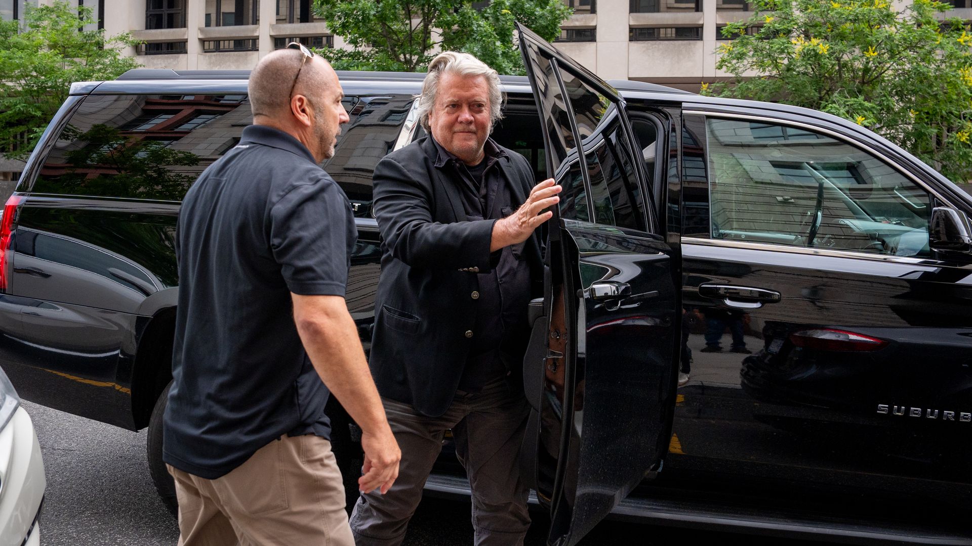 Bannon exits a black car. Another person is stepping in front of him.