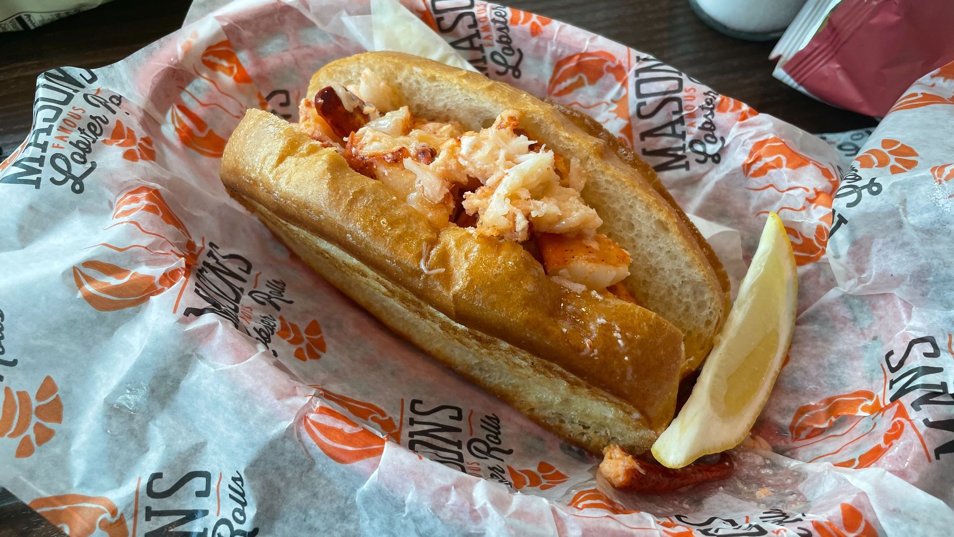 A lobster roll, which includes a toasted bun with lobster meat stacked inside it, and a lemon wedge.