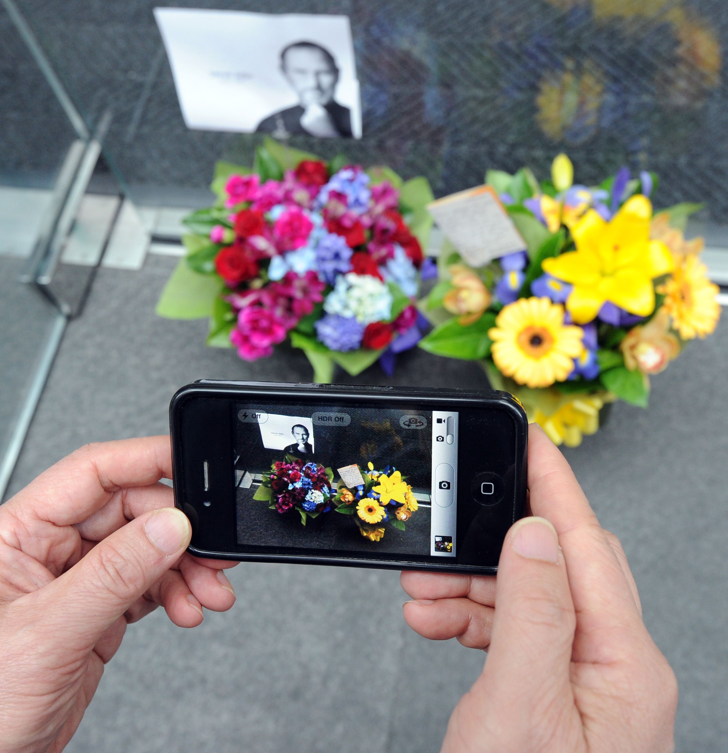 A passerby uses an iPhone 4 to photograph flowers left for the late Steve Jobs, co-founder of Apple, outside the Apple store in Sydney on October 6, 2011.