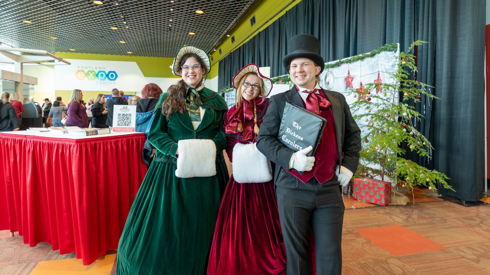 A photo of three people dressed in caroler garb and smiling.