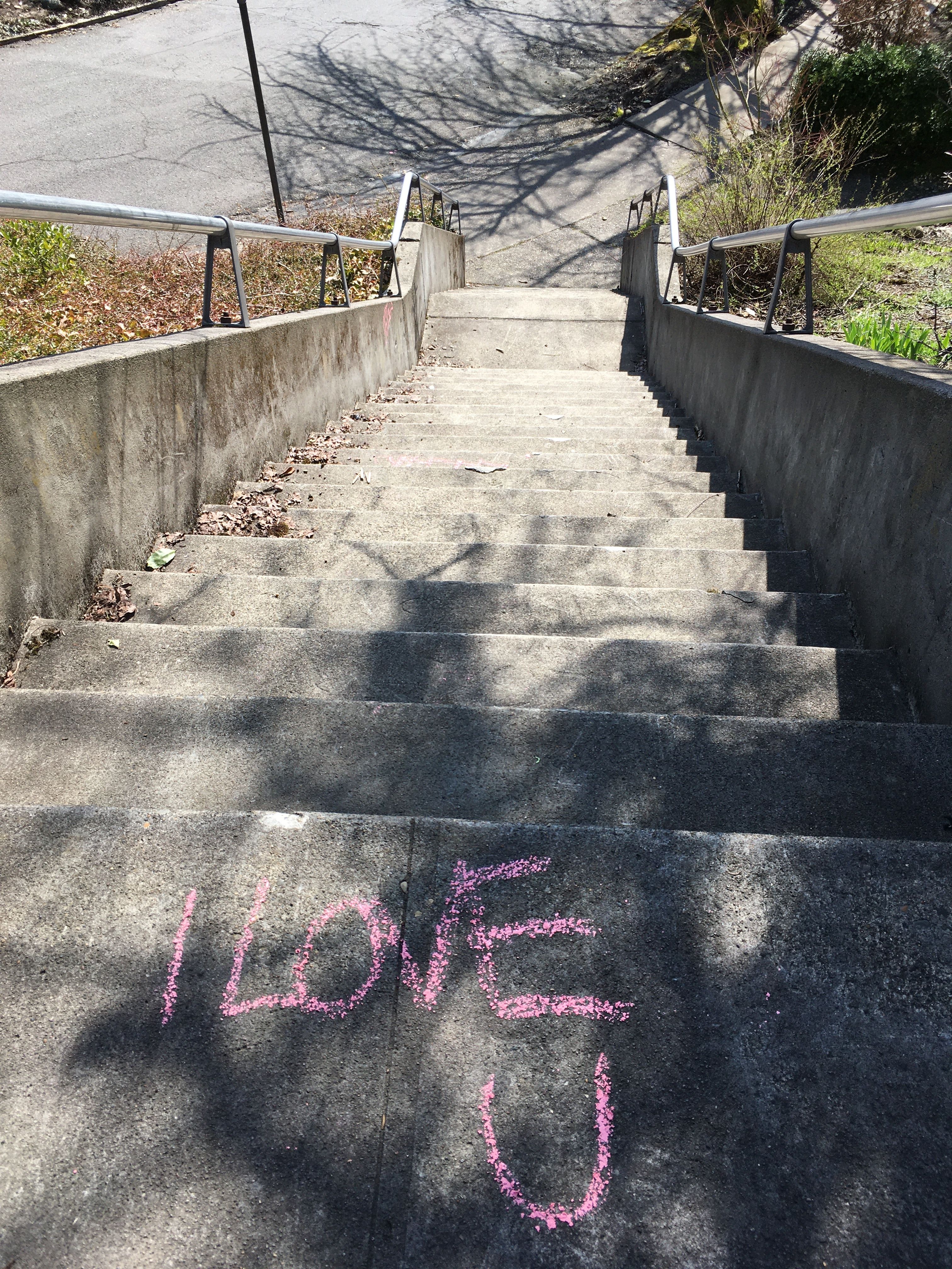 I love you is written in pink chalk at the top of a set of concrete steps.