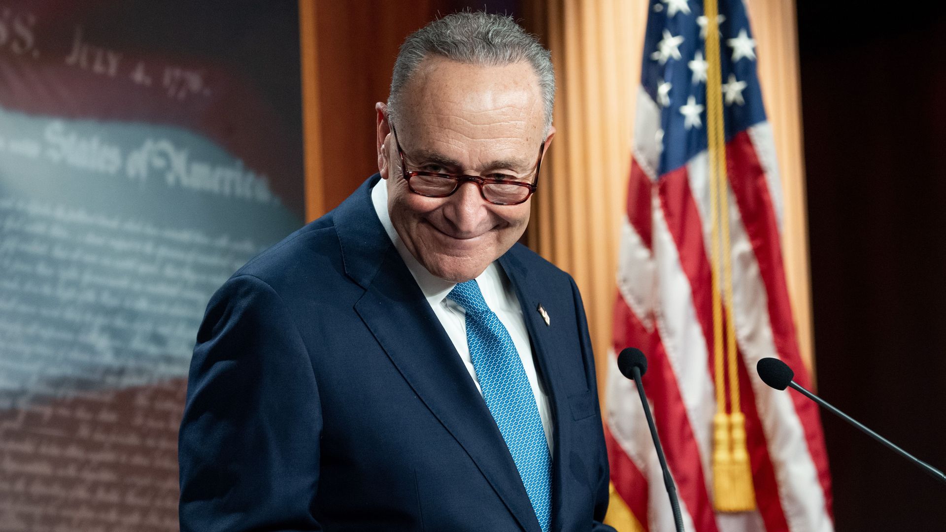 Senate Minority Leader Chuck Schumer smiling at a podium