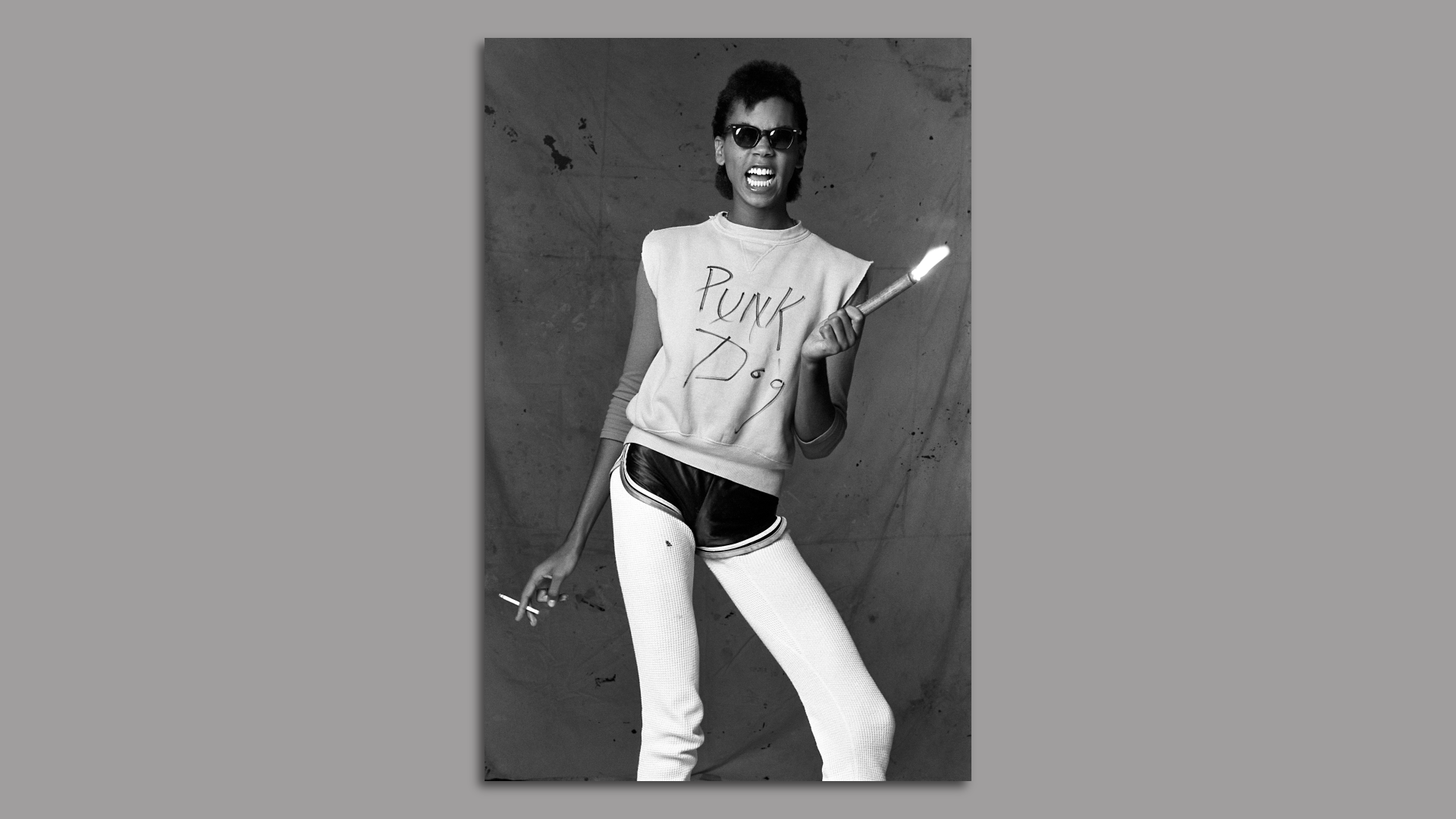 A black and white photo of a young RuPaul wearing sunglasses and a shirt with the words "Punk dog" while holding a flare and cigarette