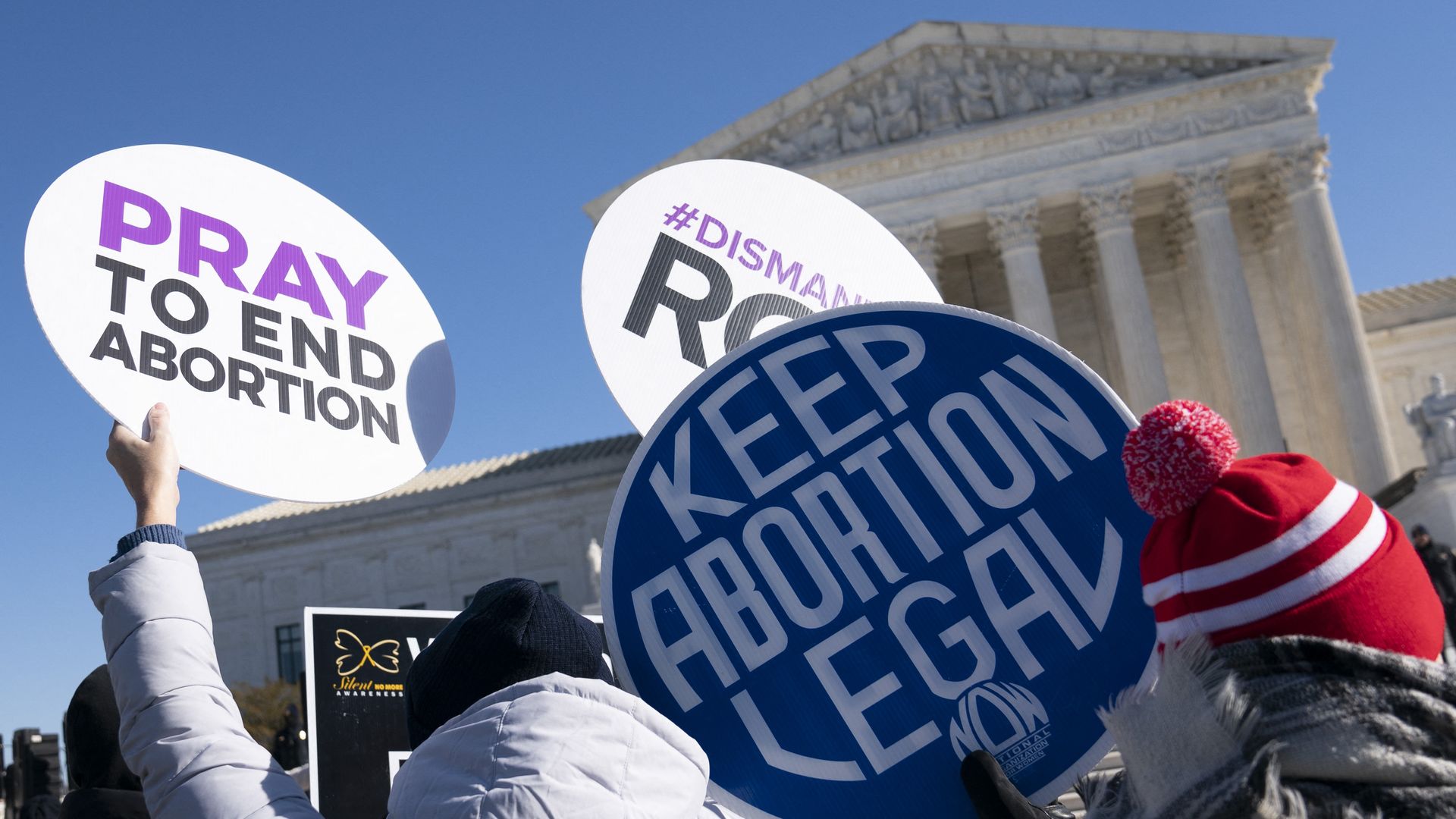 Picture of the Supreme Court building with people in front of it holding signs that say "pray to end abortion" and "keep abortion legal"
