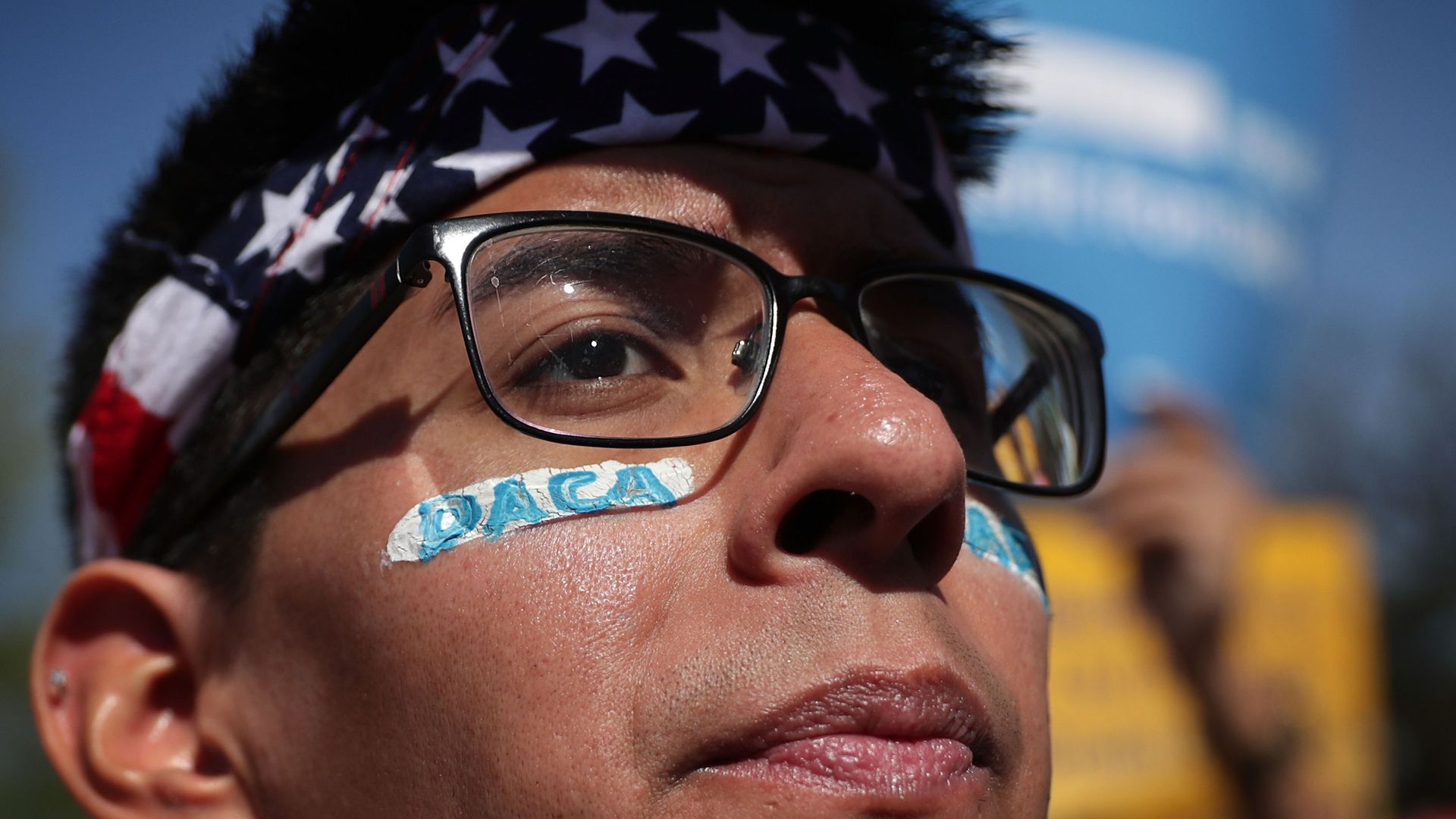 DACA protestor with glasses, American flag bandana and stickers under his eyes with "DACA" written on them
