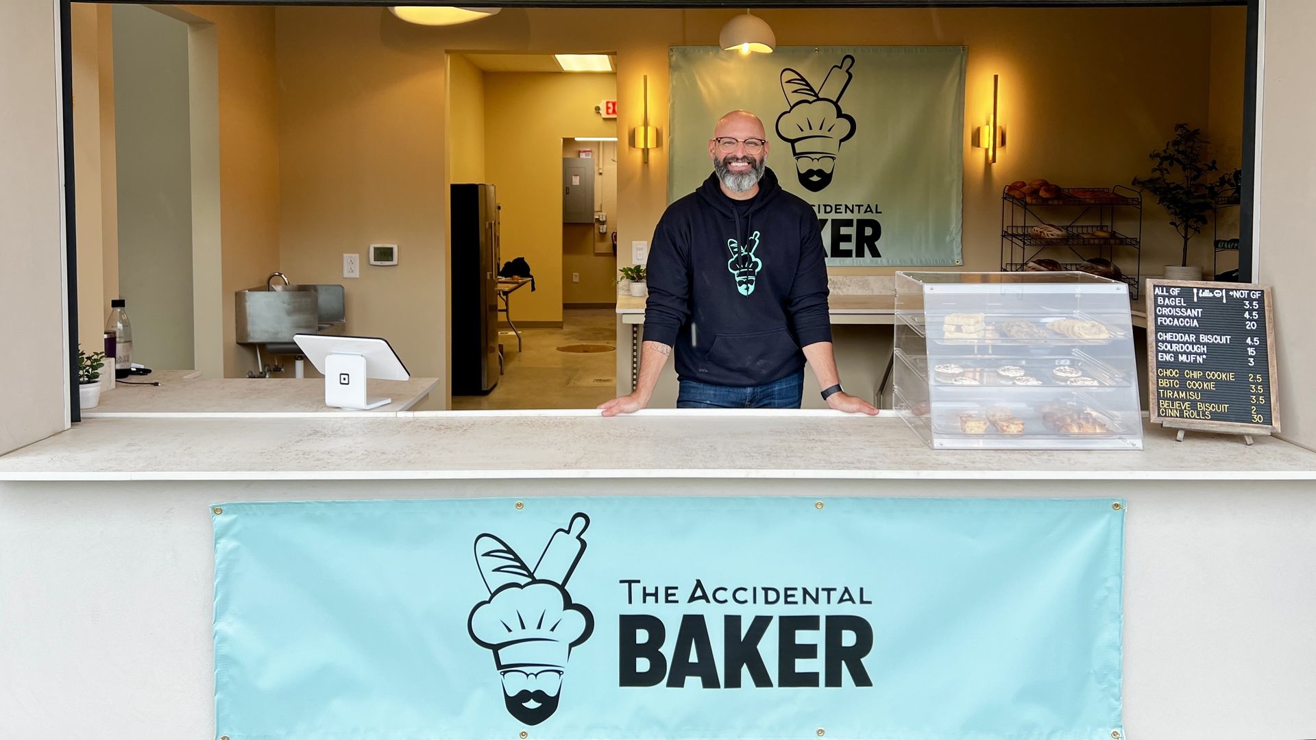 man stands behind pop-up window, a banner sign that reads "the accidental baker" is below him