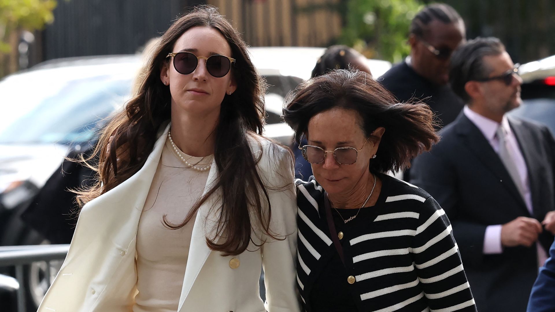 Businesswoman Charlie Javice (L), with long, dark hair, dark sunglasses, a cream jacket, top, pants and a white pearl necklace, arrives for her sentencing hearing at federal court in Manhattan, New York City, accompanied by a woman with shoulder-length dark hair, sunglasses and a black-white top.