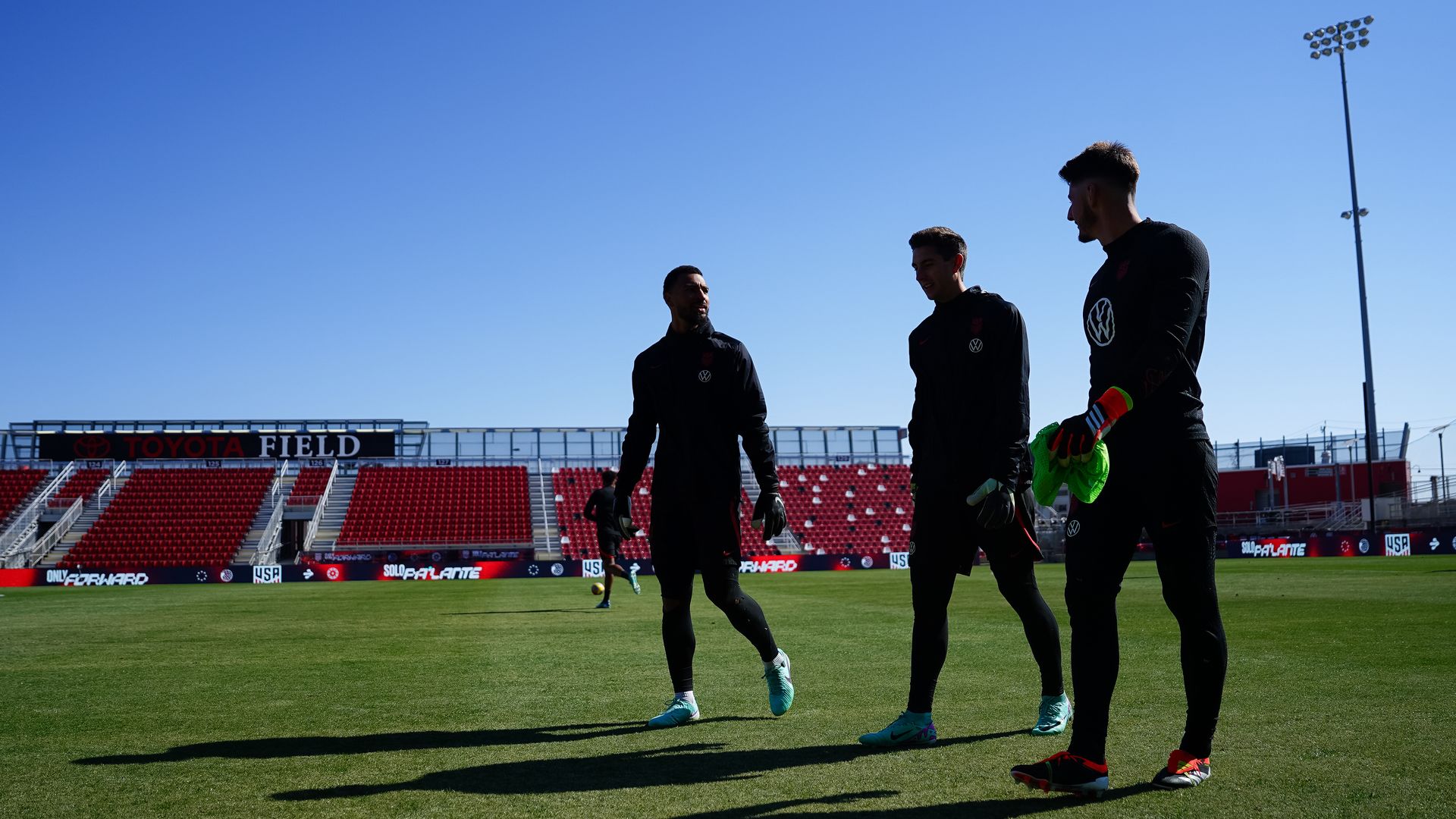 Three soccer players walk off a field.