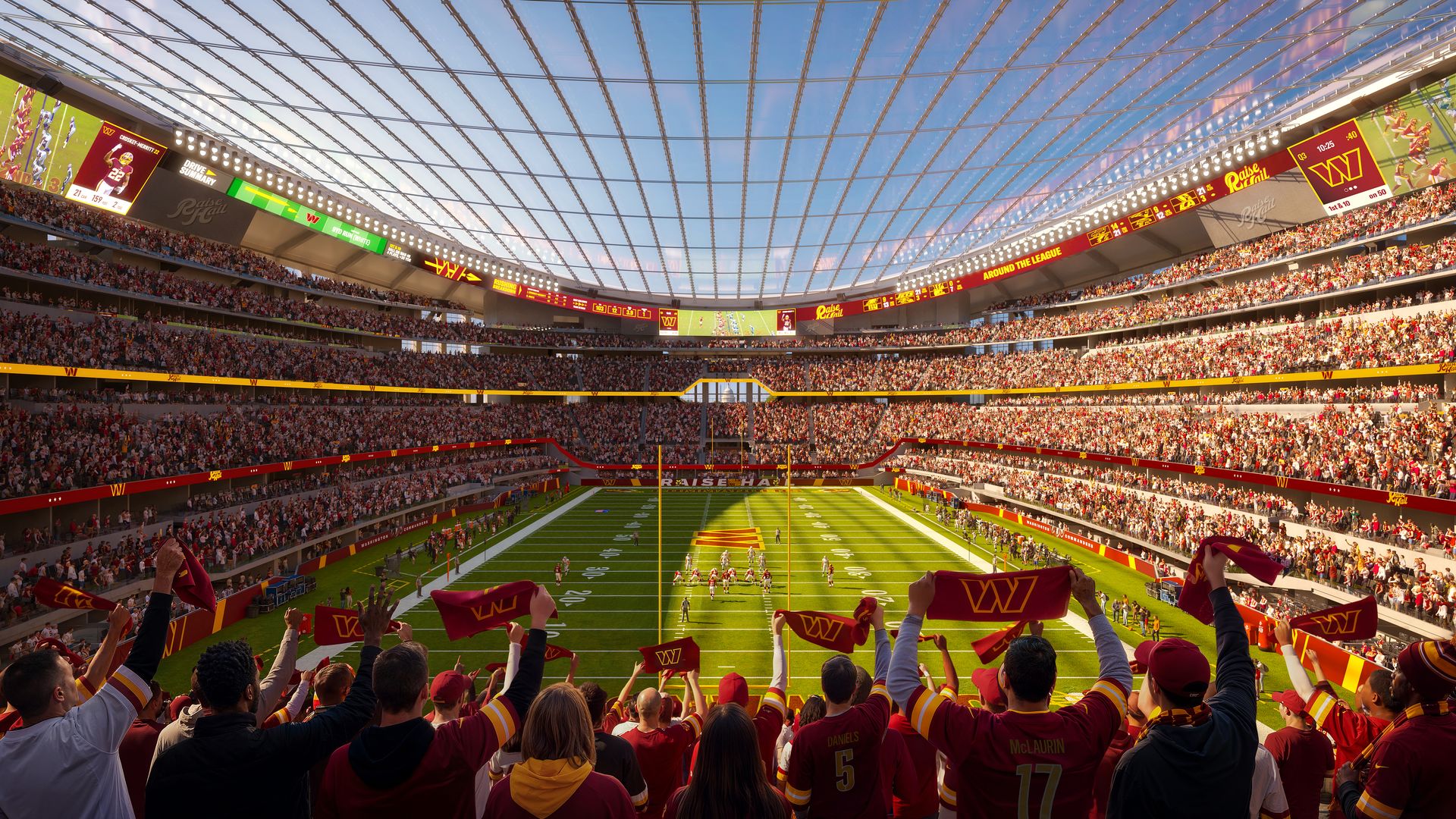 Large football stadium packed with fans in red and gold, waving towels. Players on the green field beneath a glass roof and bright scoreboards circling the stands.