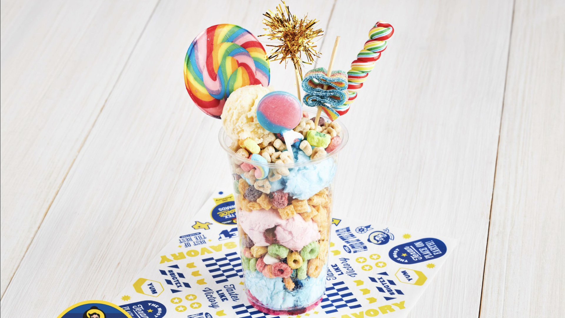 A cup with cotton candy, sweet cereal, pickles and sour candy