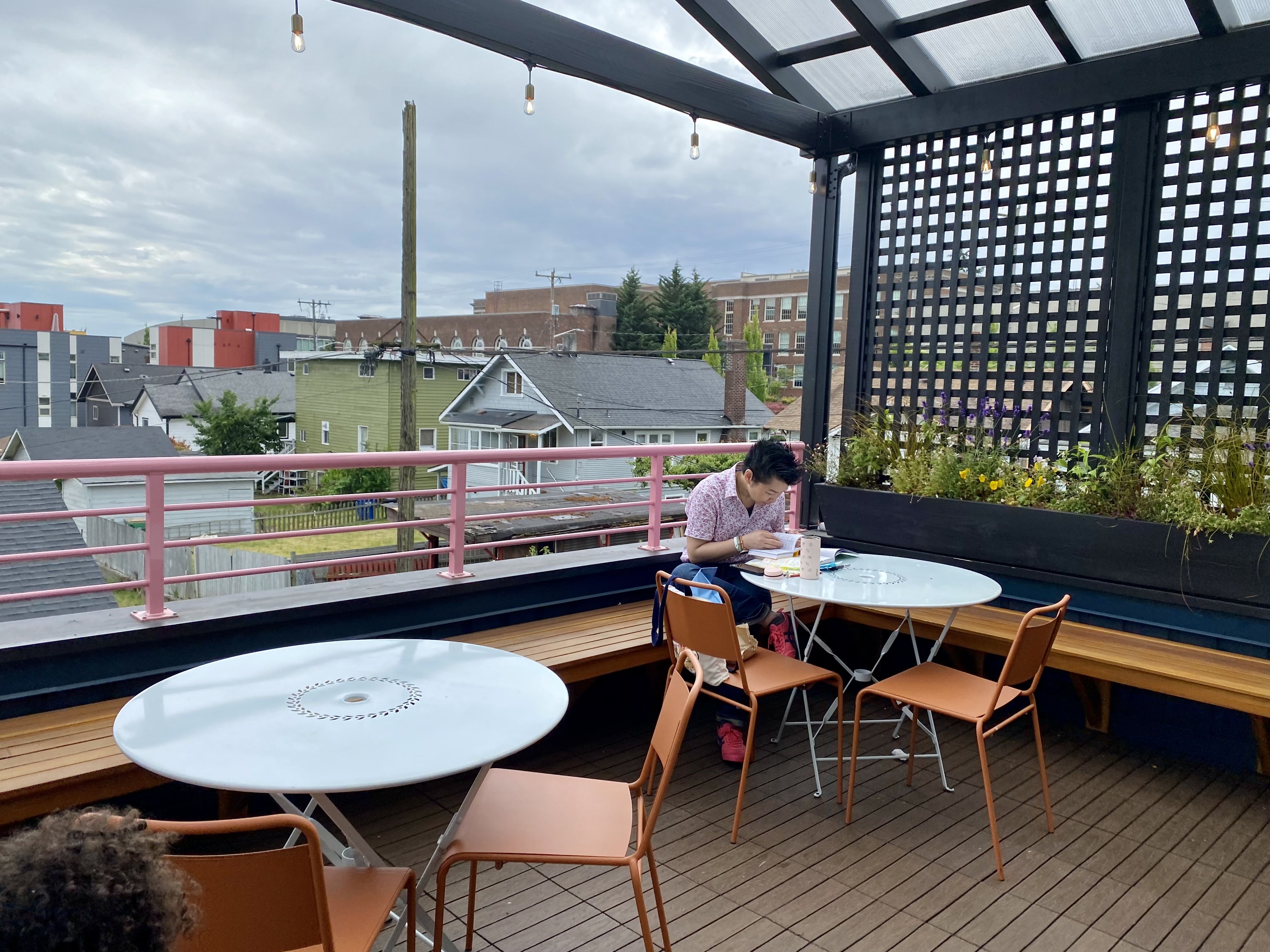 Someone sits at a round cafe table on the rooftop deck of Flora Bakehouse, which overlooks the neighborhood.