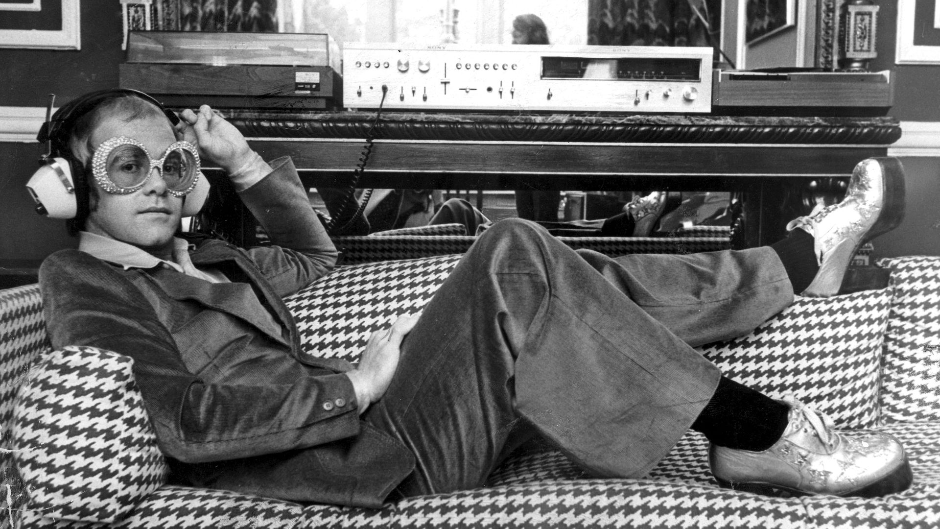 Elton John lounging on a couch and listening to music
